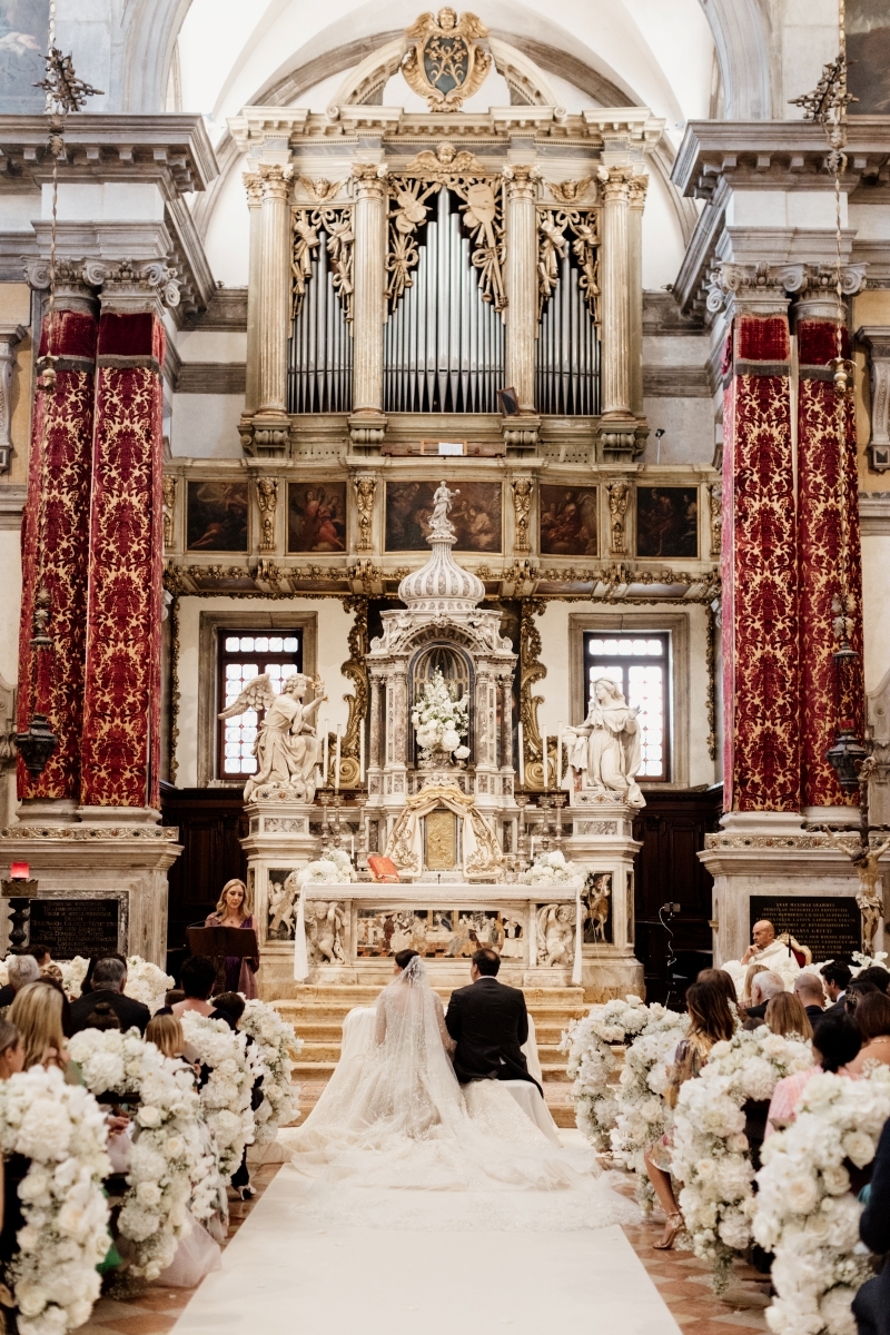 Bride and groom at the altar in a church decorated with flowers and a white walkway in the center - ACCAELLE Events | Organizzazione eventi e Wedding planner