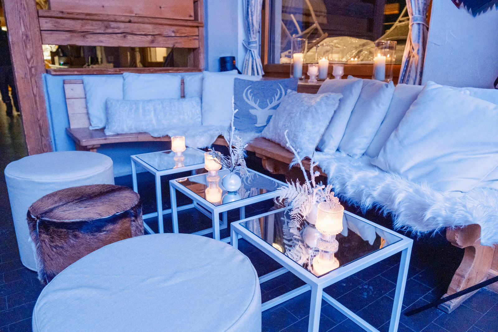 Cozy lounge area set up for a mountain event, with wooden benches, white cushions and faux furs - ACCAELLE Events | Organizzazione eventi e Wedding planner
