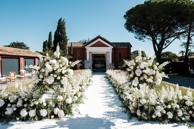 Wedding ceremony setup with white flowers and a red and white building in the background - ACCAELLE Events | Organizzazione eventi e Wedding planner