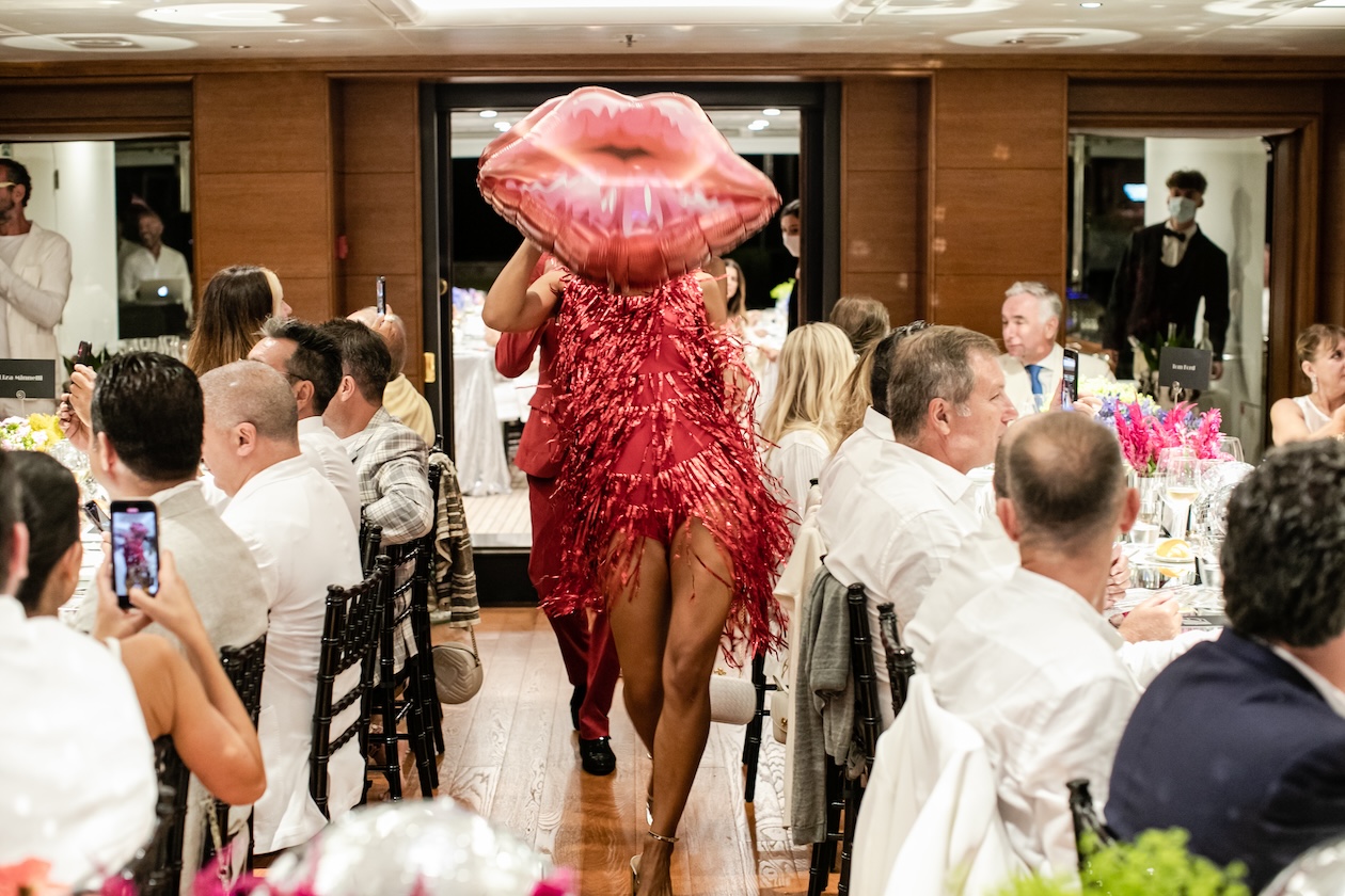 Artist in red dress and extravagant headdress walking among seated guests - ACCAELLE Events | Organizzazione eventi e Wedding planner