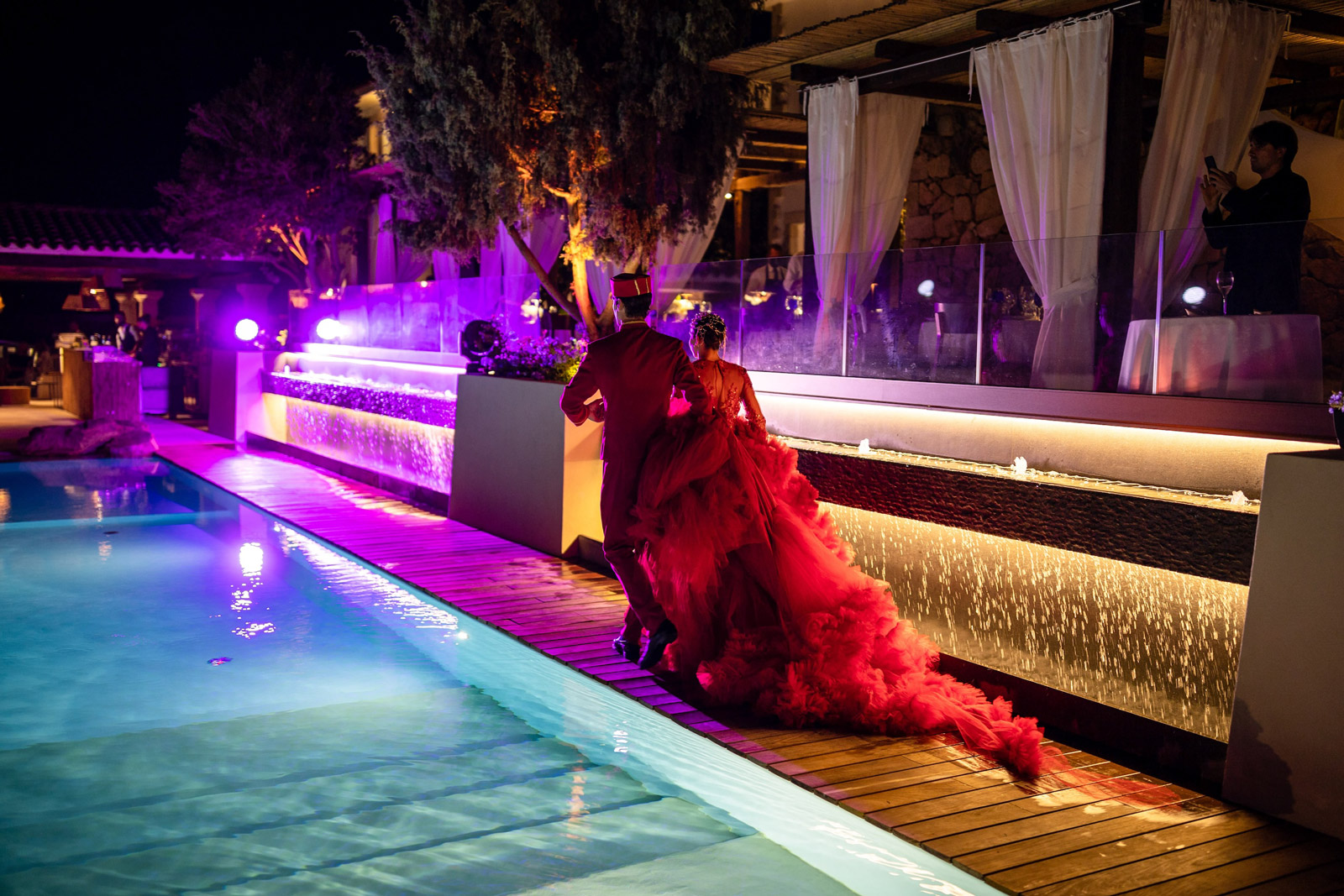 Artists in red dresses walking along the poolside - ACCAELLE Events | Organizzazione eventi e Wedding planner