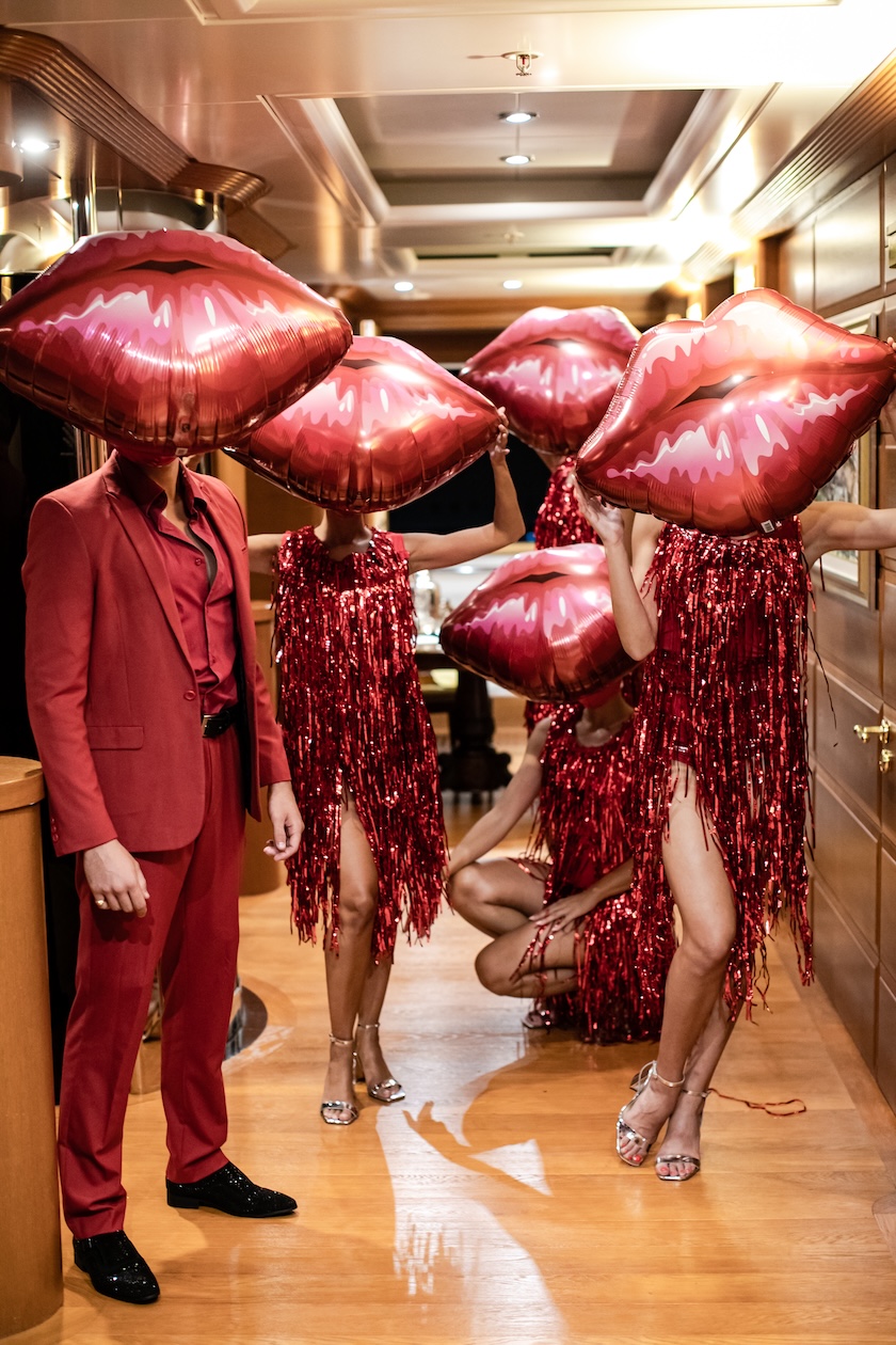 Artists in red robes with lip-shaped headdresses pose in a corridor - ACCAELLE Events | Organizzazione eventi e Wedding planner