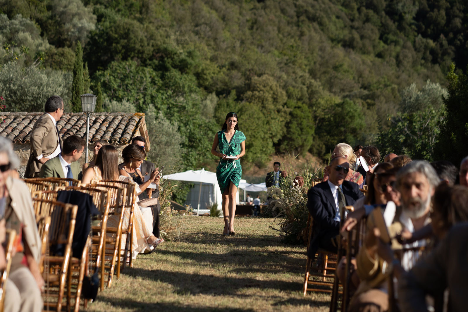 A bridesmaid walks down the aisle at an outdoor wedding ceremony surrounded by guests. - ACCAELLE Events | Organizzazione eventi e Wedding planner