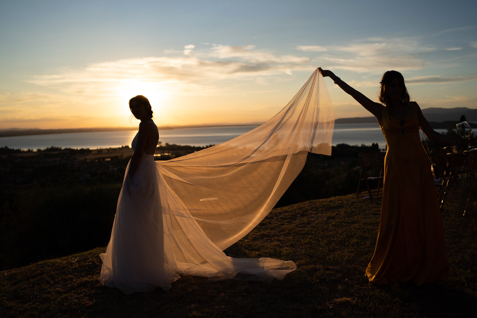 Bridesmaid holding bride's wedding dress in her hand in the evening - ACCAELLE Events | Organizzazione eventi e Wedding planner