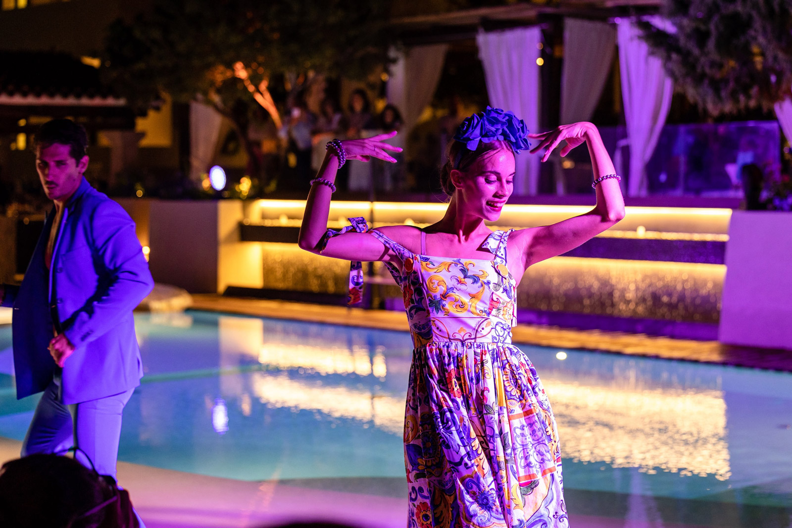 Woman dancing happily near a swimming pool illuminated by purple lights in the evening. - ACCAELLE Events | Organizzazione eventi e Wedding planner