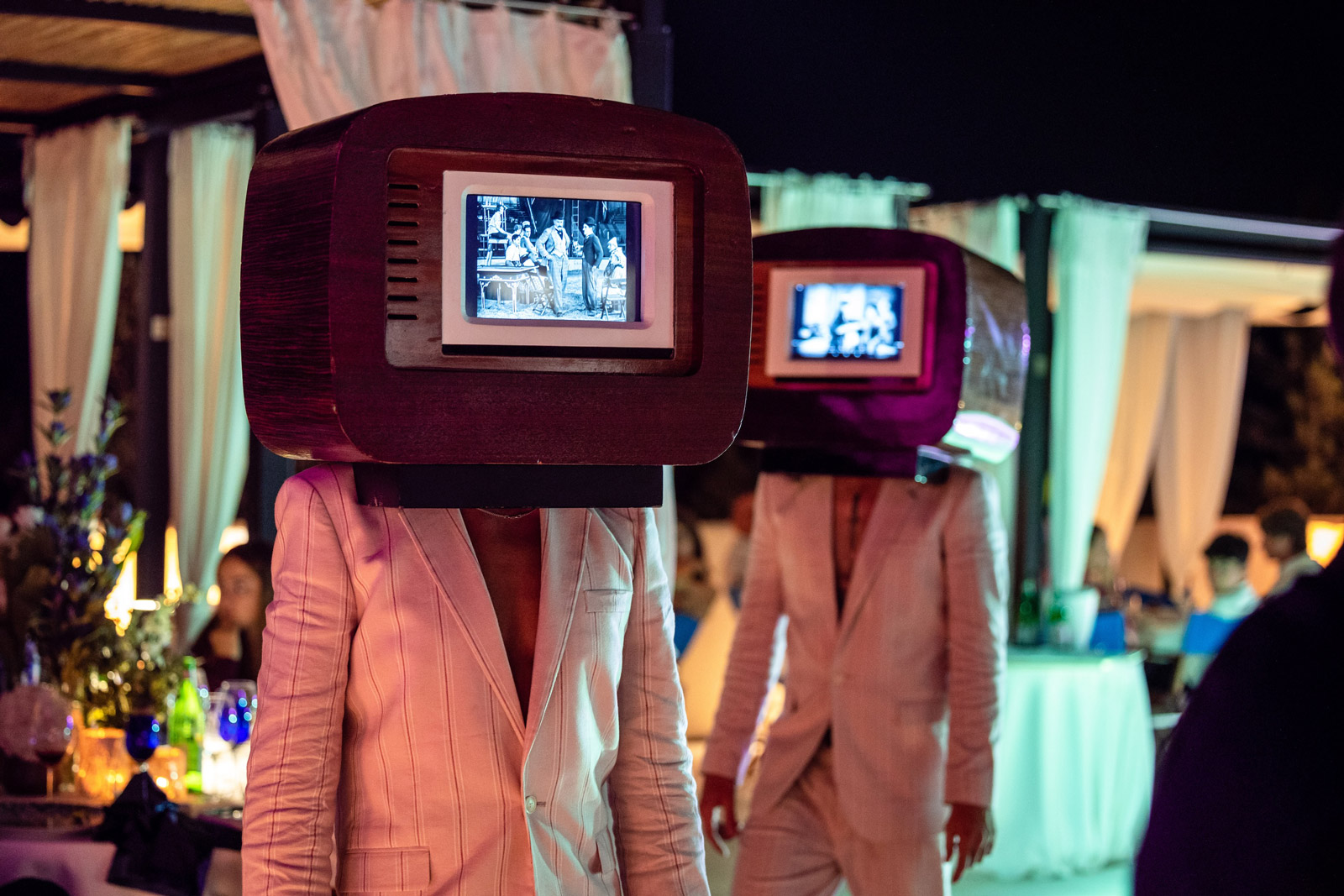 Two artists in light jackets with illuminated vintage televisions instead of heads. - ACCAELLE Events | Organizzazione eventi e Wedding planner