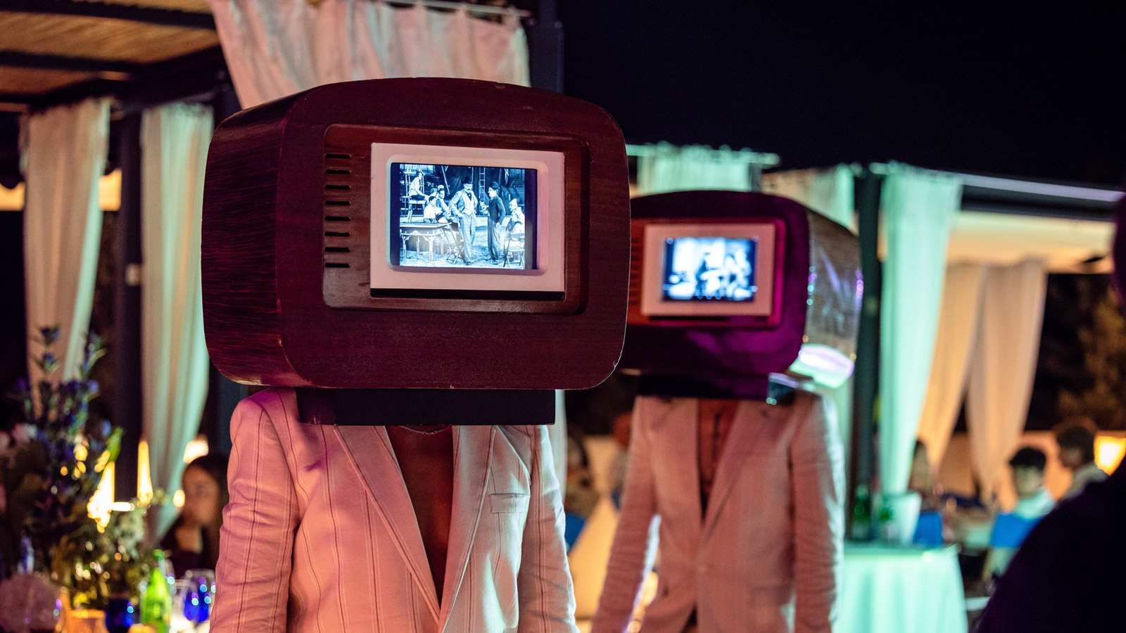 Two performers in white jackets with old vintage televisions for heads at an evening event. - ACCAELLE Events | Organizzazione eventi e Wedding planner