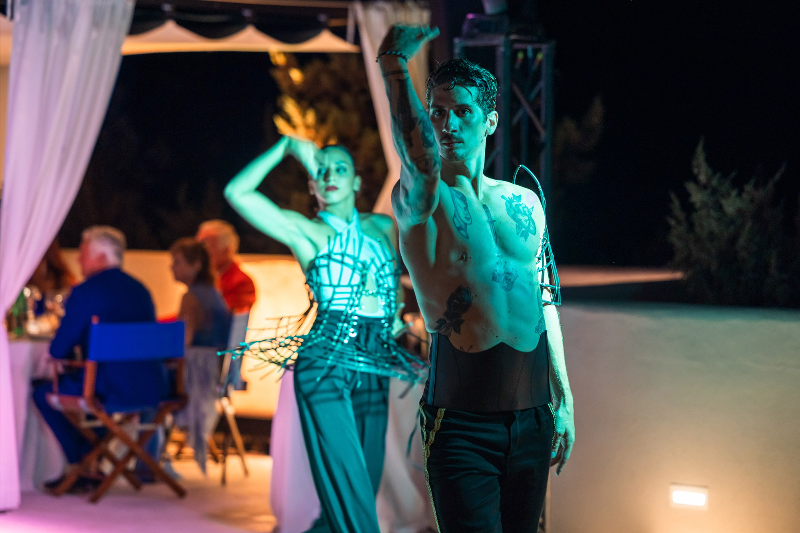 Two people dancing with their arms raised under colored lights in the evening - ACCAELLE Events | Organizzazione eventi e Wedding planner