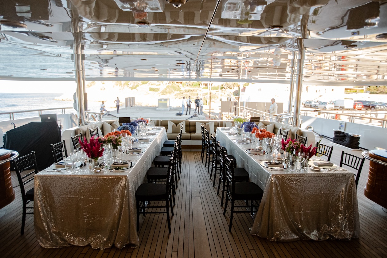 Two mirrored rectangular tables set up on the covered veranda of the yacht. - ACCAELLE Events | Organizzazione eventi e Wedding planner