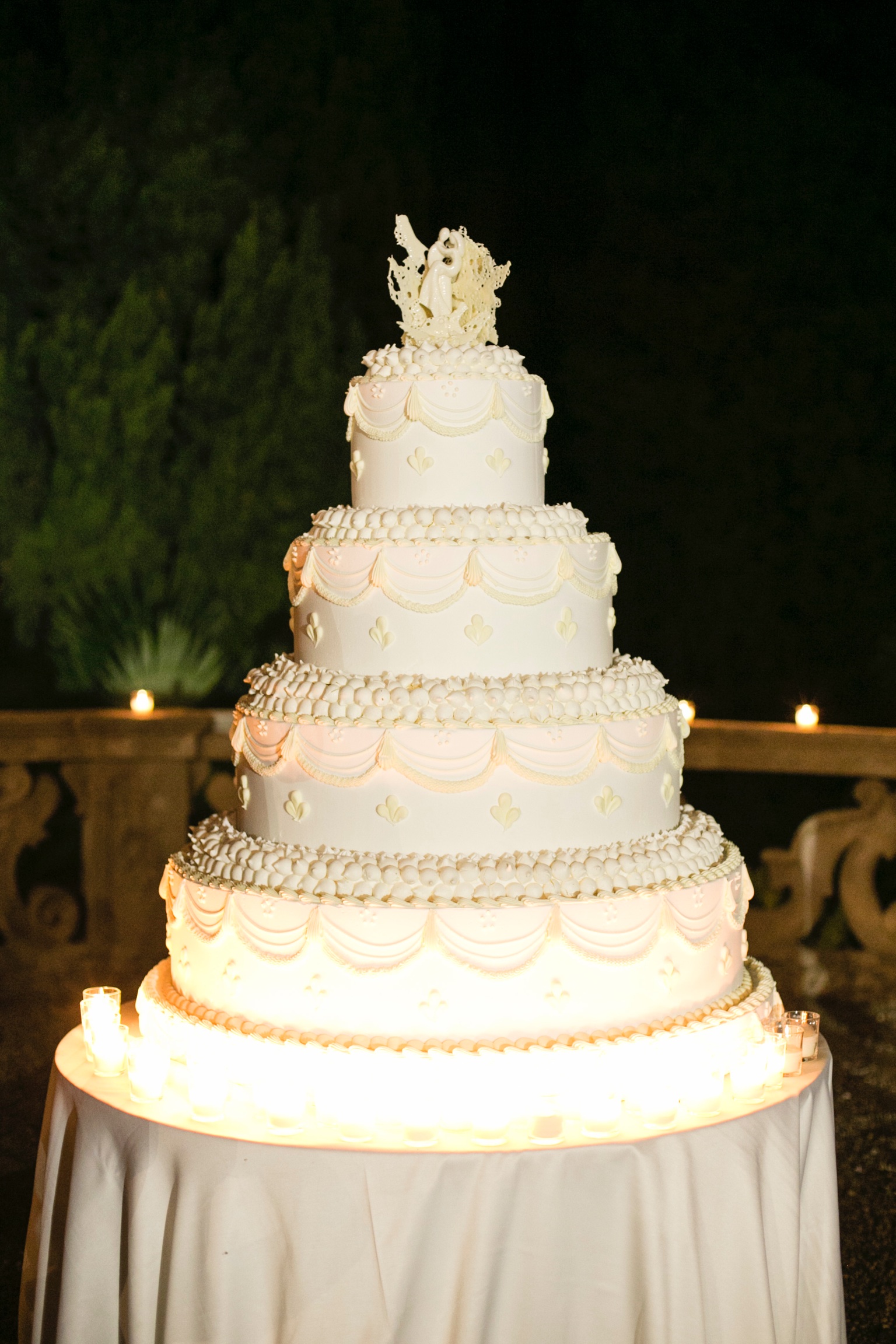 Large, tiered, white, illuminated wedding cake on a table ready for the evening cutting. - ACCAELLE Events | Organizzazione eventi e Wedding planner