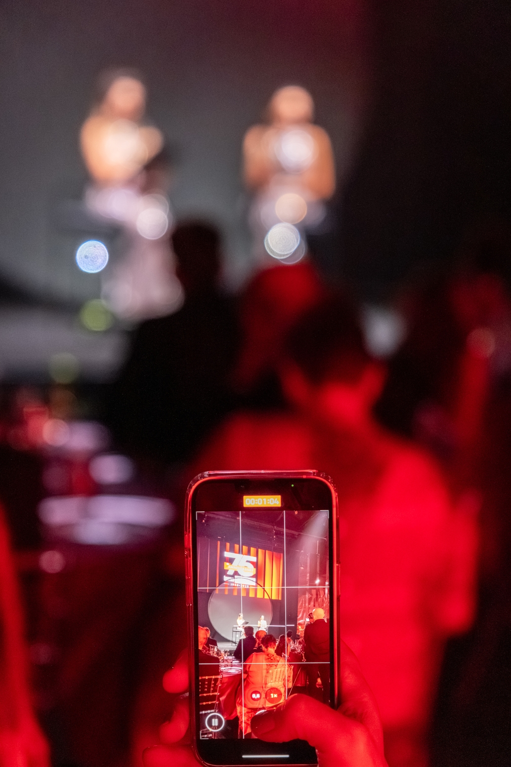 Guest recording the show with his smartphone in a red-lit room. - ACCAELLE Events | Organizzazione eventi e Wedding planner