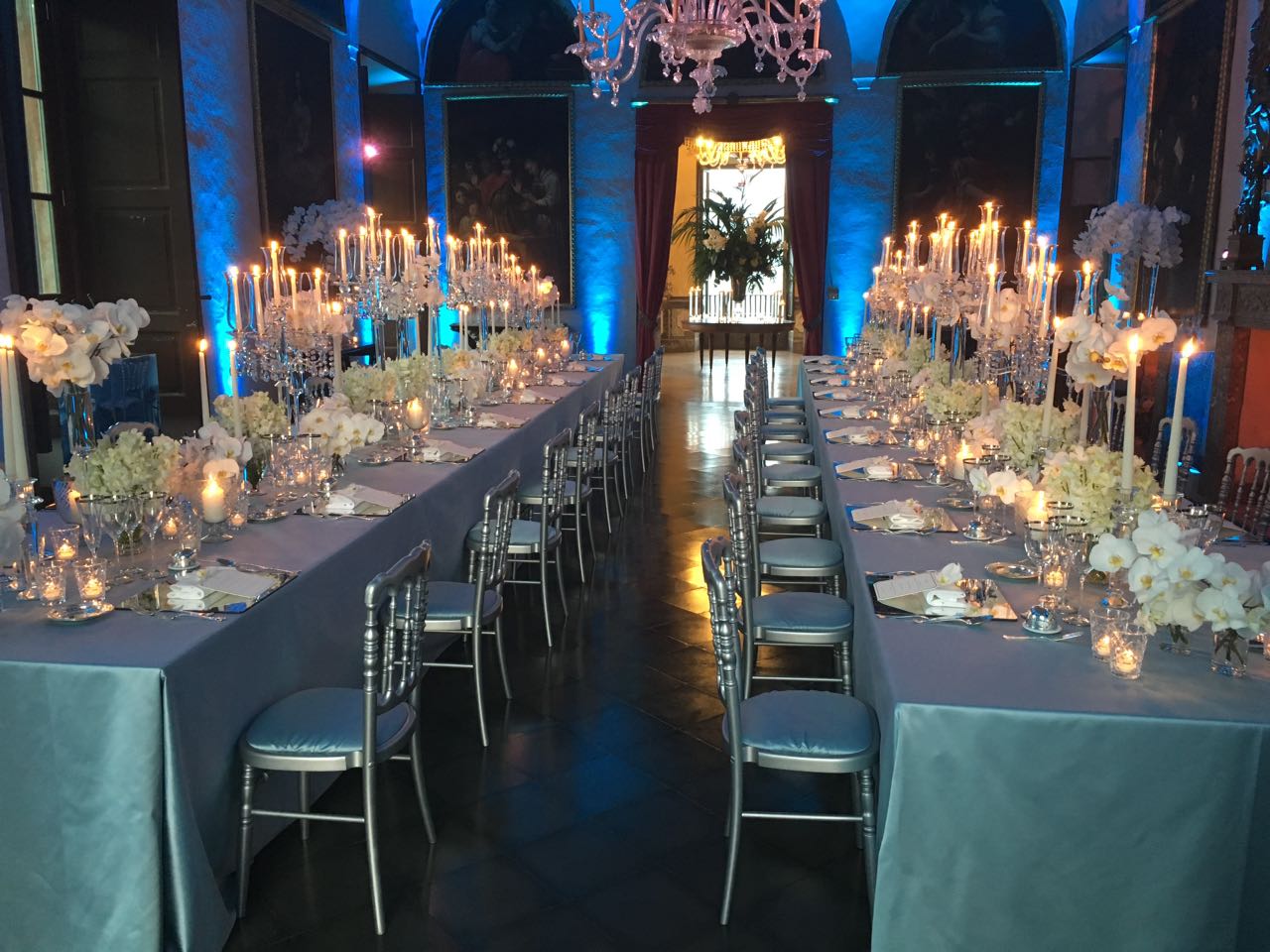 Long table set up in a historic room with candles and blue lighting - ACCAELLE Events | Organizzazione eventi e Wedding planner