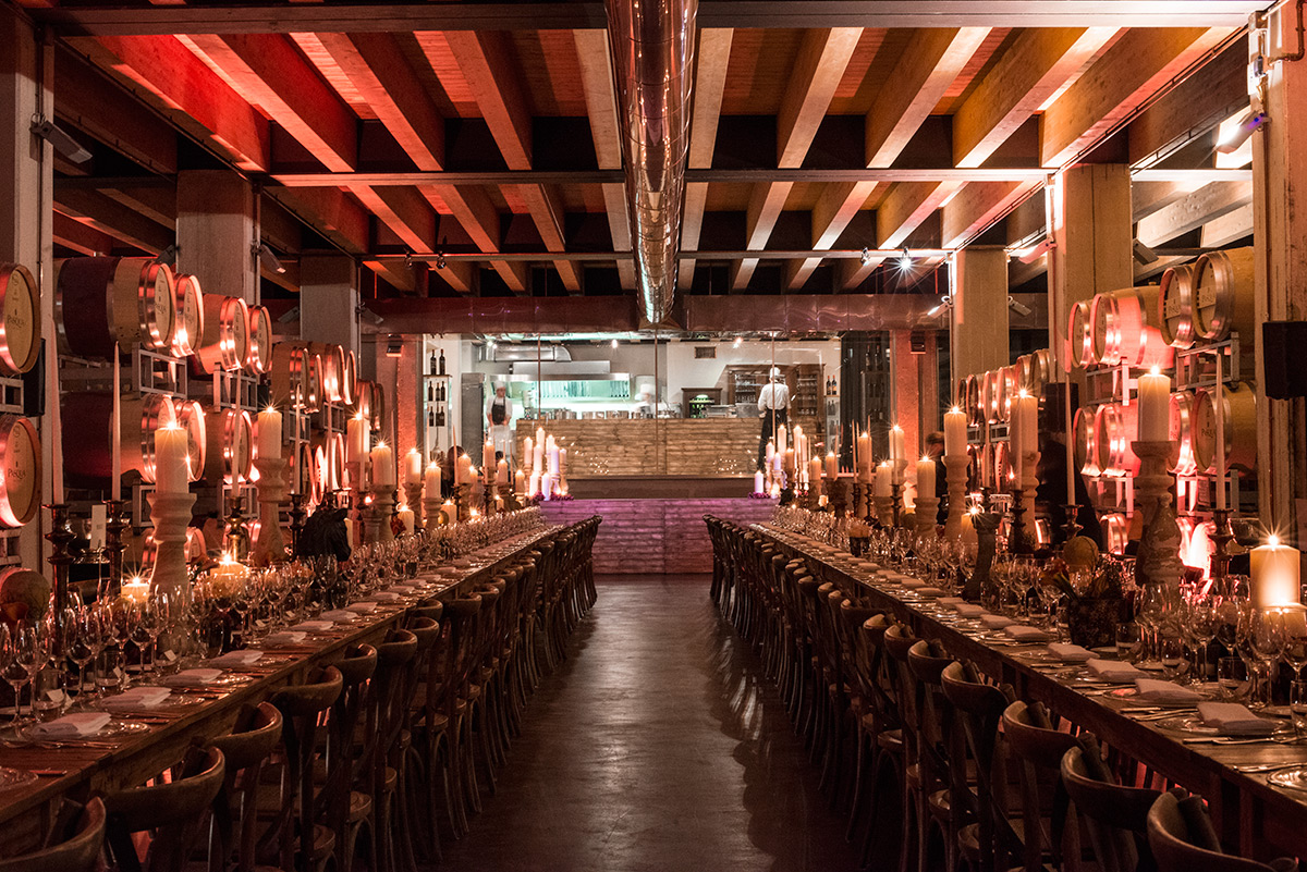 Long tables set up for an event inside a cellar with wooden barrels. - ACCAELLE Events | Organizzazione eventi e Wedding planner