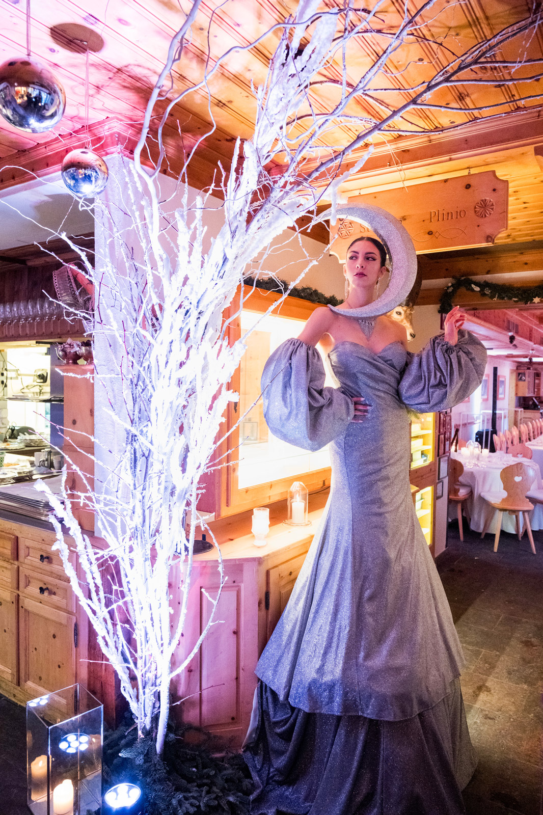 Model in elegant grey glitter evening dress with eye-catching moon-shaped headpiece, posing next to bright branches - ACCAELLE Events | Organizzazione eventi e Wedding planner