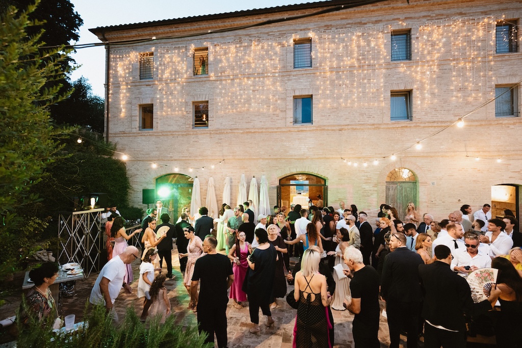 Wedding guests in the evening, building decorated with warm lights in the background - ACCAELLE Events | Organizzazione eventi e Wedding planner
