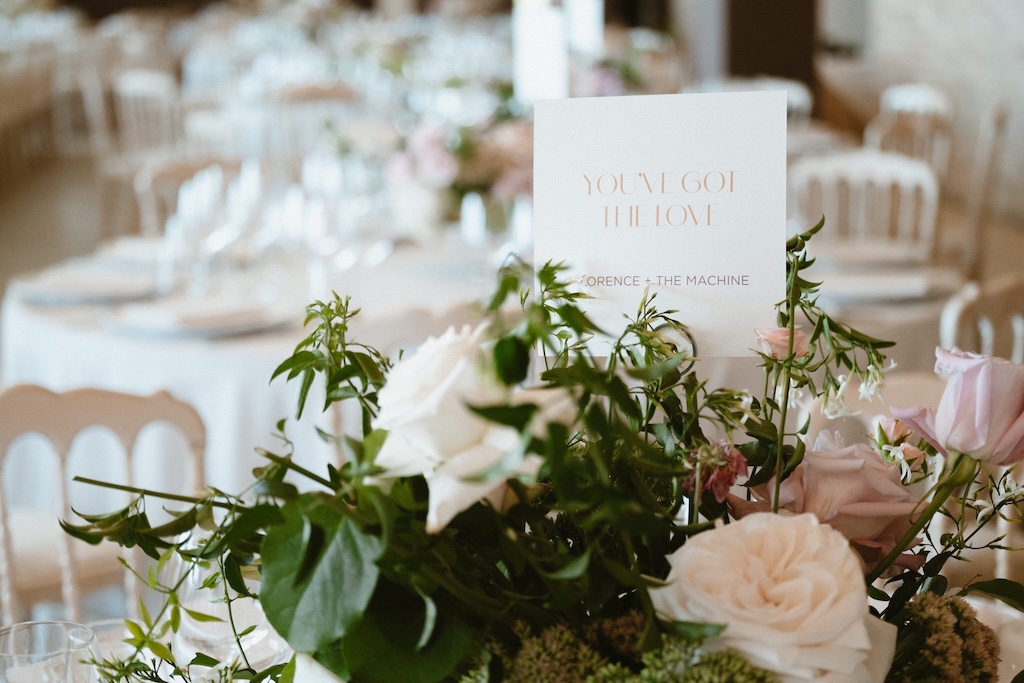 Close-up of a bouquet of roses with a welcome card placed on top in the center and tables in the background - ACCAELLE Events | Organizzazione eventi e Wedding planner