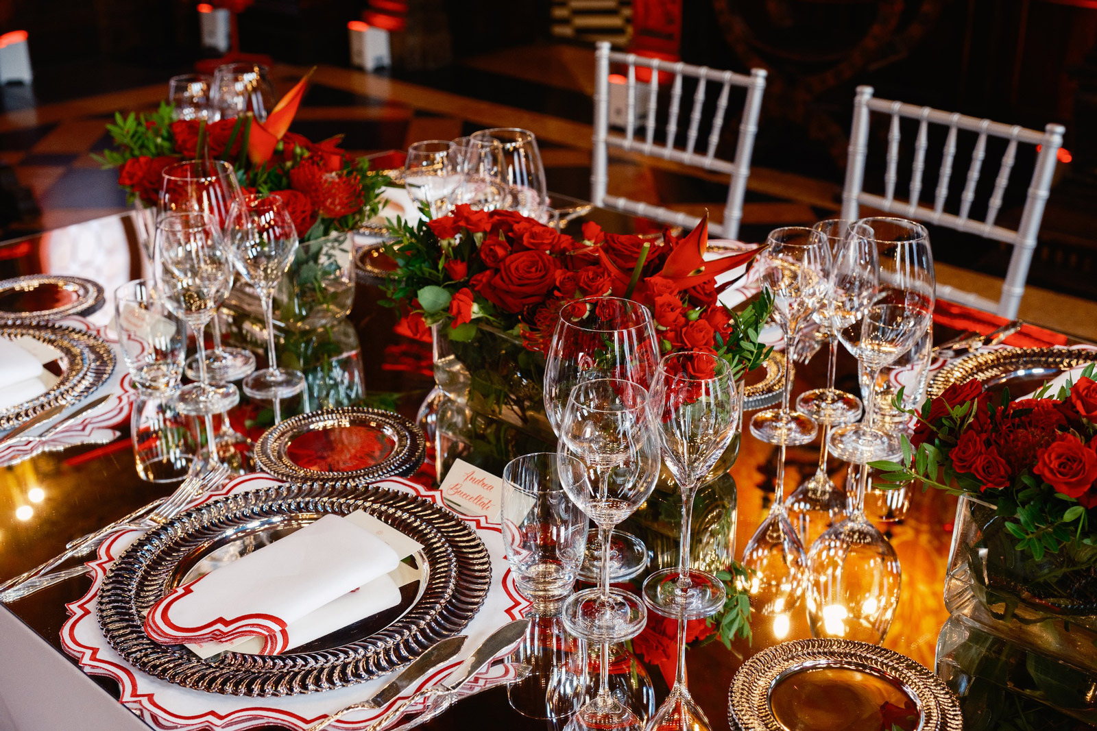 Close-up of crystal glasses, reflective plates and a rich centerpiece of red roses - ACCAELLE Events | Organizzazione eventi e Wedding planner
