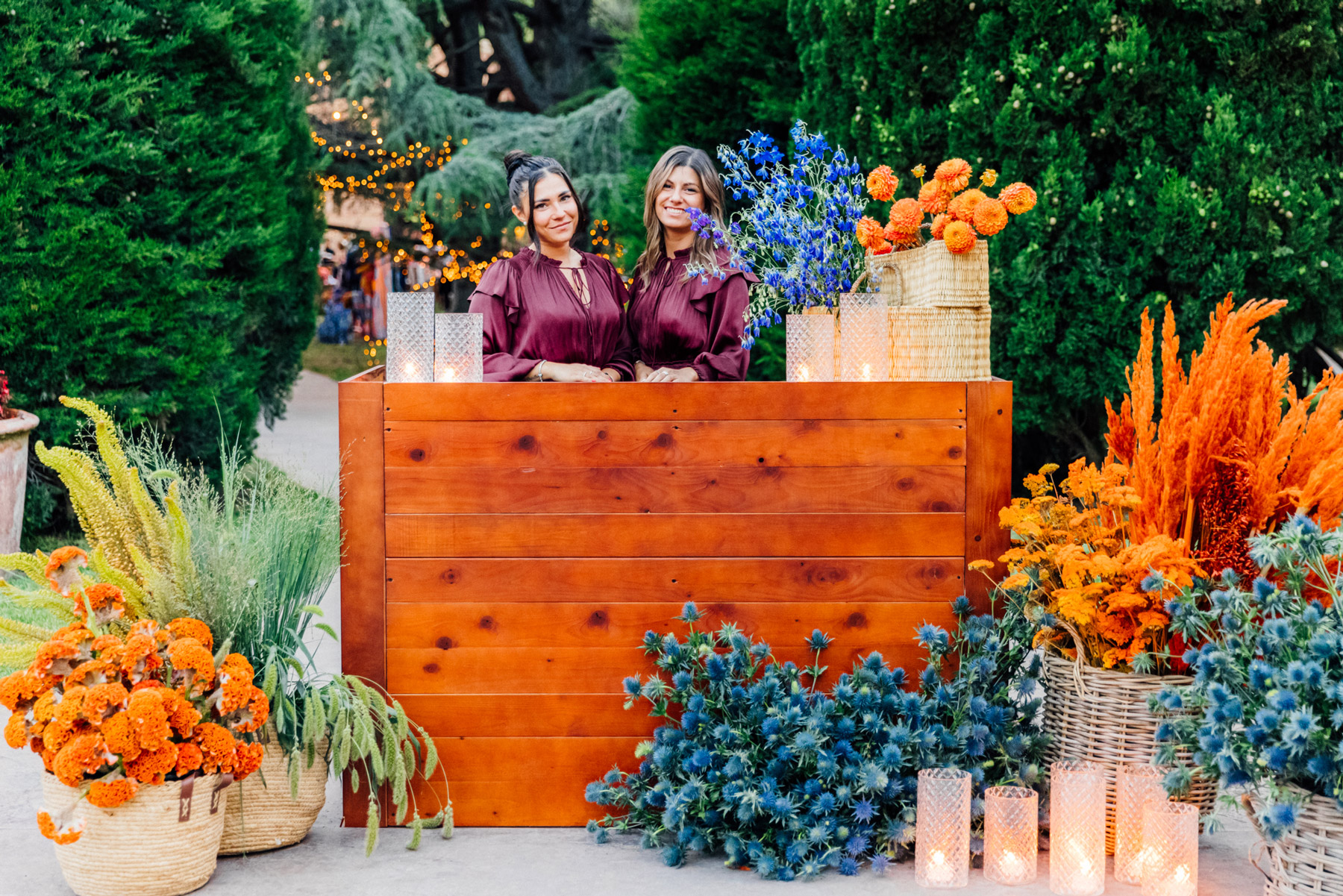 Girls posing behind a wooden counter with flowers of various colors scattered around - ACCAELLE Events | Organizzazione eventi e Wedding planner