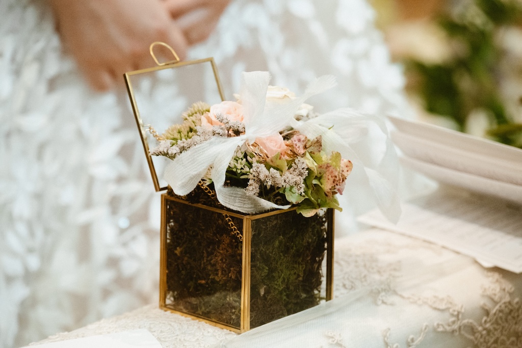 Glass cube box containing moss and white rose flowers with bride's hands in the background - ACCAELLE Events | Organizzazione eventi e Wedding planner