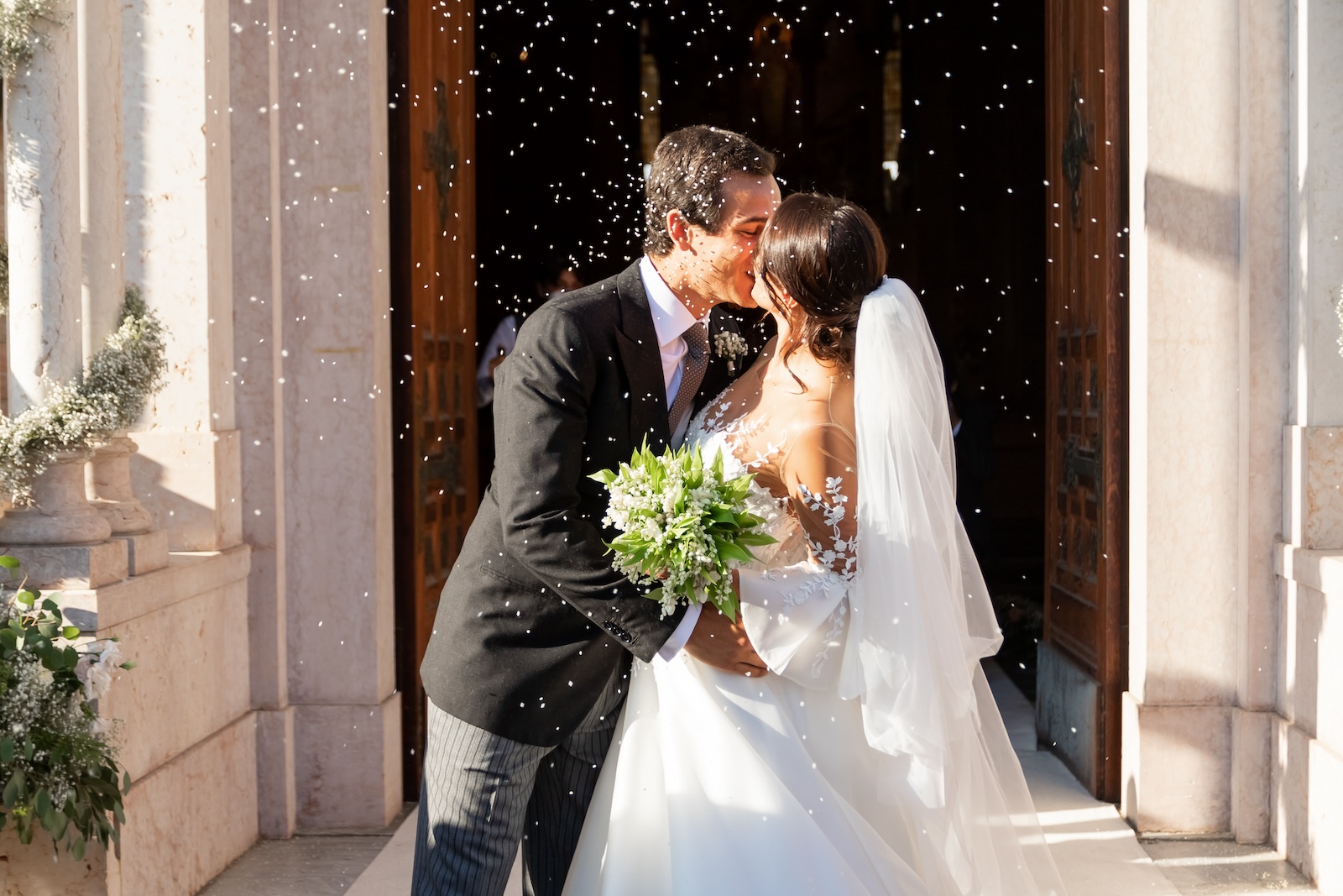 Newlyweds kissing romantically in front of the entrance of a church - ACCAELLE Events | Organizzazione eventi e Wedding planner