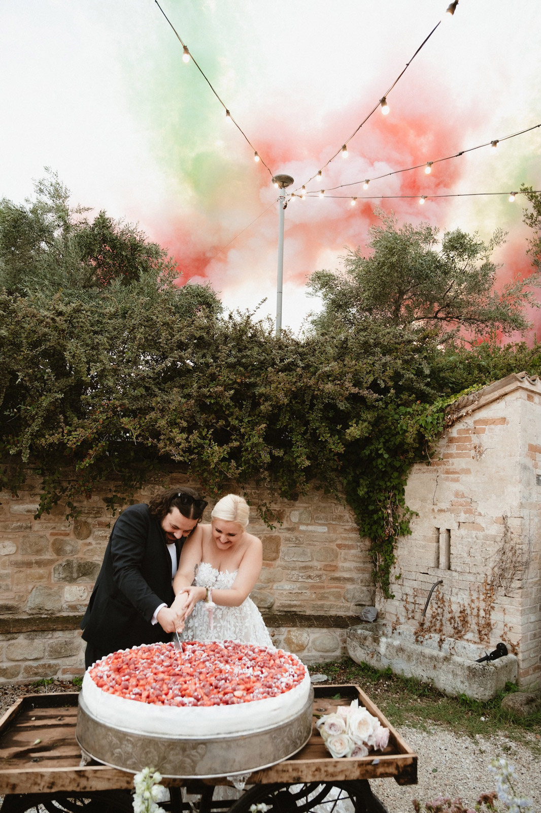 Bride and groom cutting the wedding cake with colored smoke bombs in the sky - ACCAELLE Events | Organizzazione eventi e Wedding planner