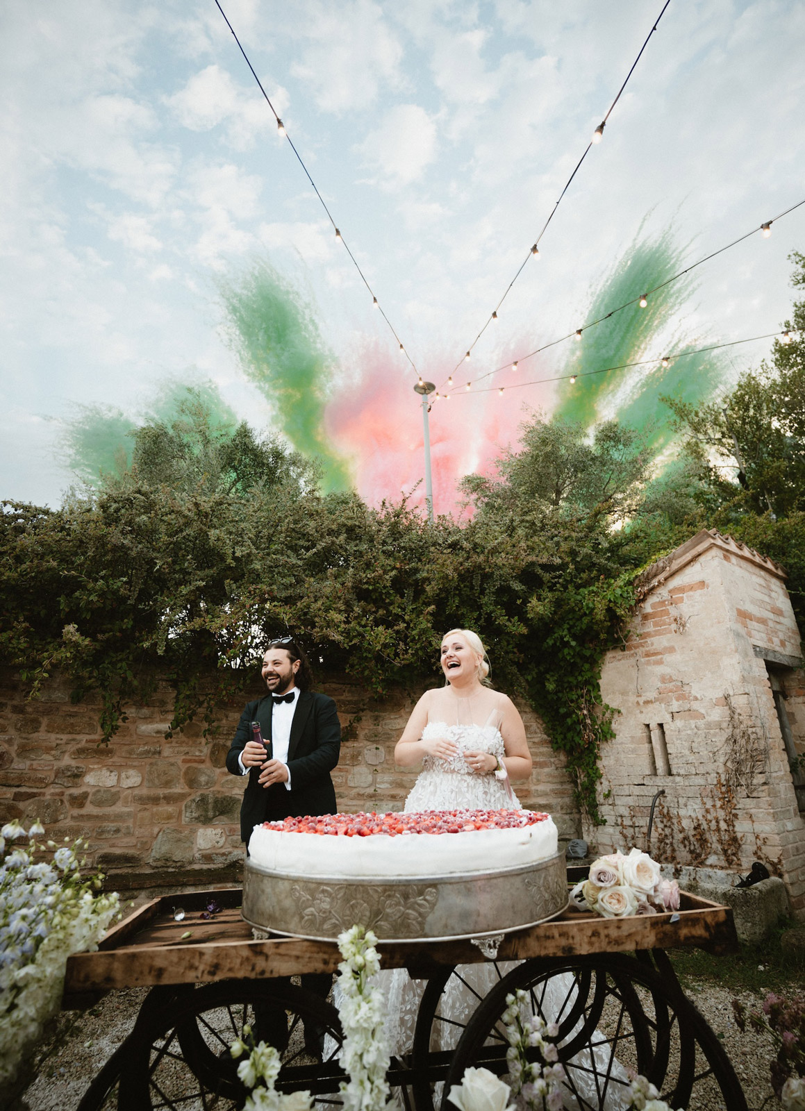 Bride and groom cutting the wedding cake with colored smoke bombs in the sky - ACCAELLE Events | Organizzazione eventi e Wedding planner