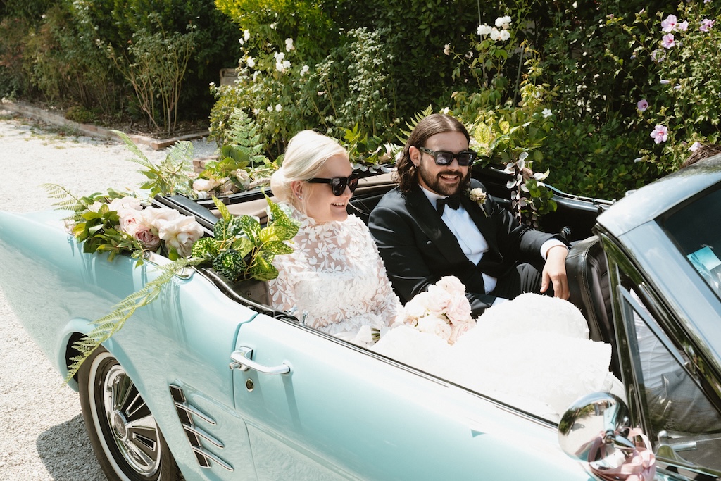 Bride and groom sitting in the blue wedding car decorated with pink and white flowers and leaves - ACCAELLE Events | Organizzazione eventi e Wedding planner