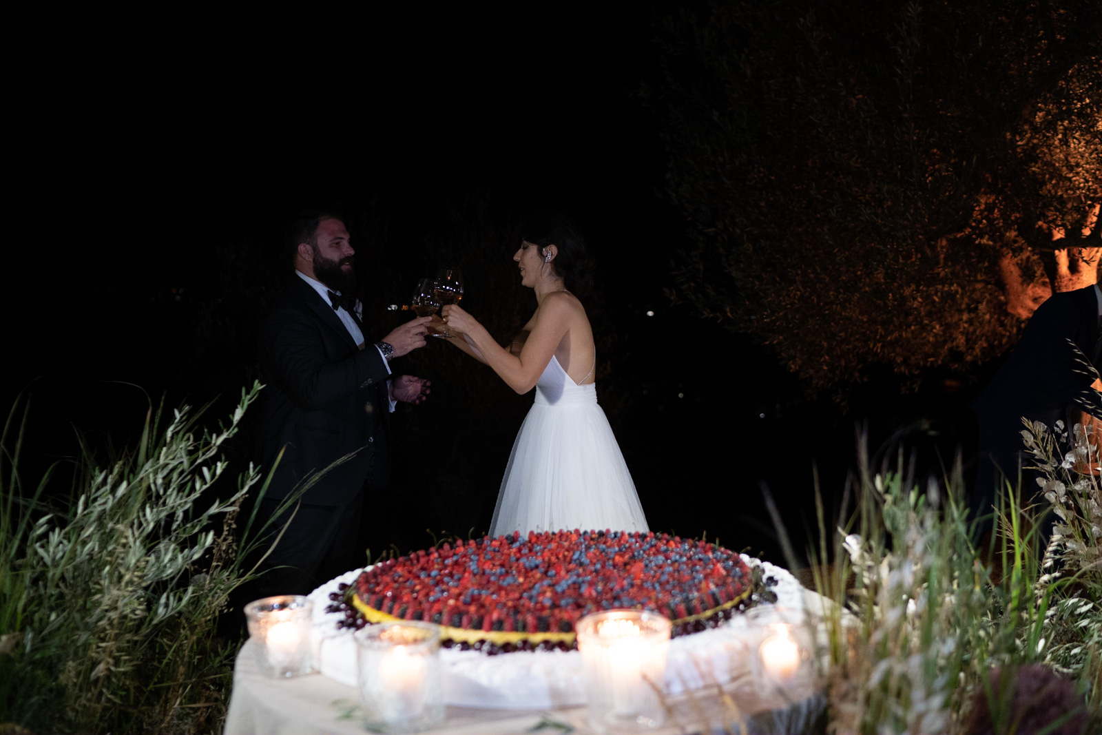 The newlyweds cut their wedding cake outdoors in the evening, illuminated by soft lights. - ACCAELLE Events | Organizzazione eventi e Wedding planner