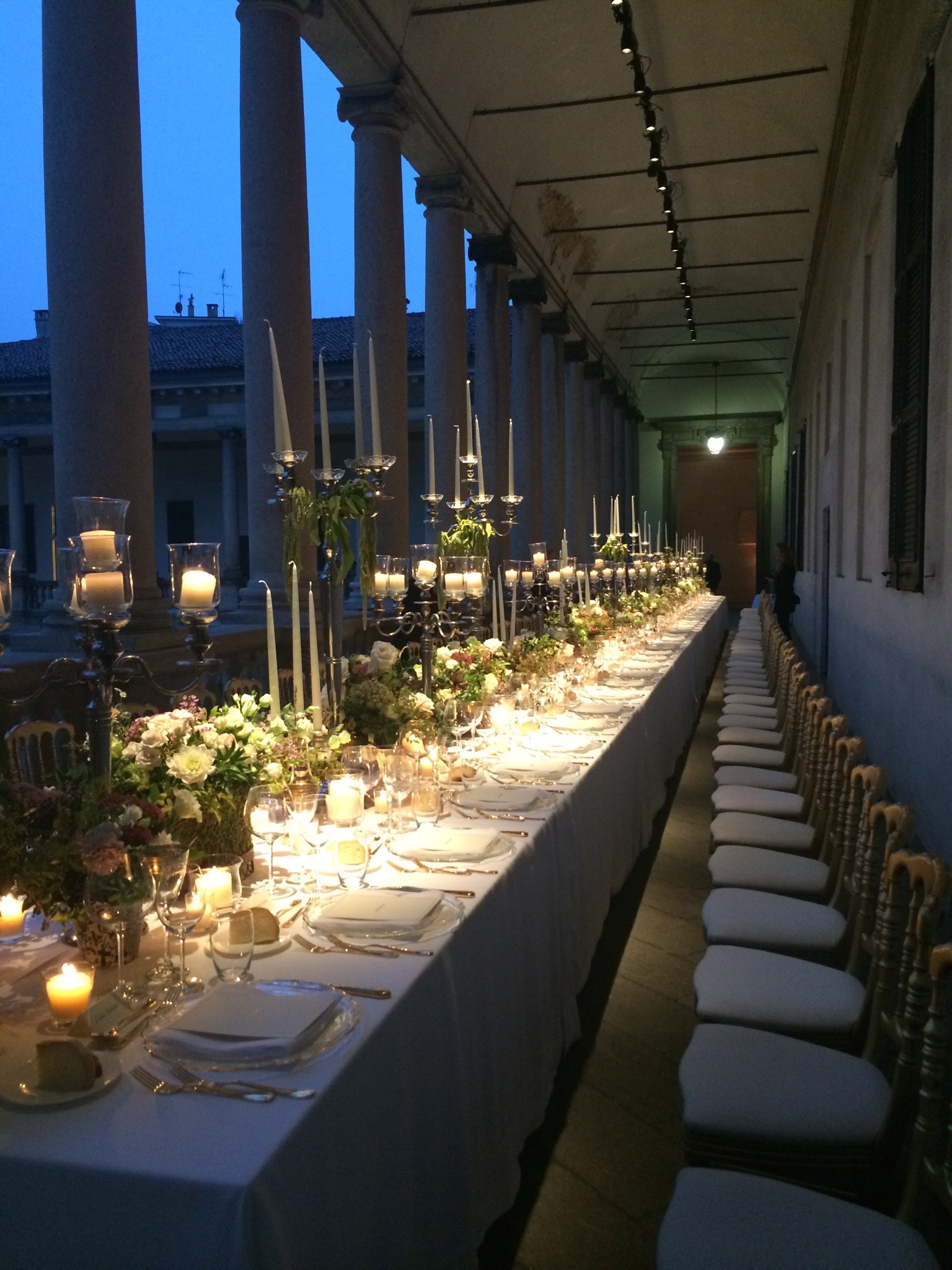 Evocative evening view of the imperial table illuminated by a row of candles under the portico. - ACCAELLE Events | Organizzazione eventi e Wedding planner
