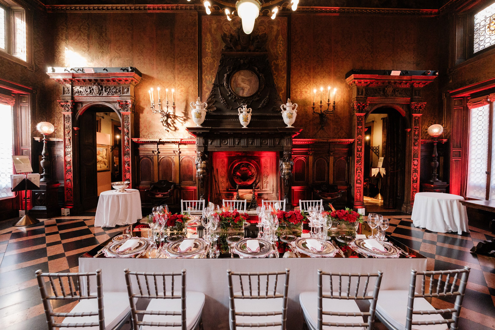 Table set in a luxurious room with a monumental fireplace and red lights. - ACCAELLE Events | Organizzazione eventi e Wedding planner