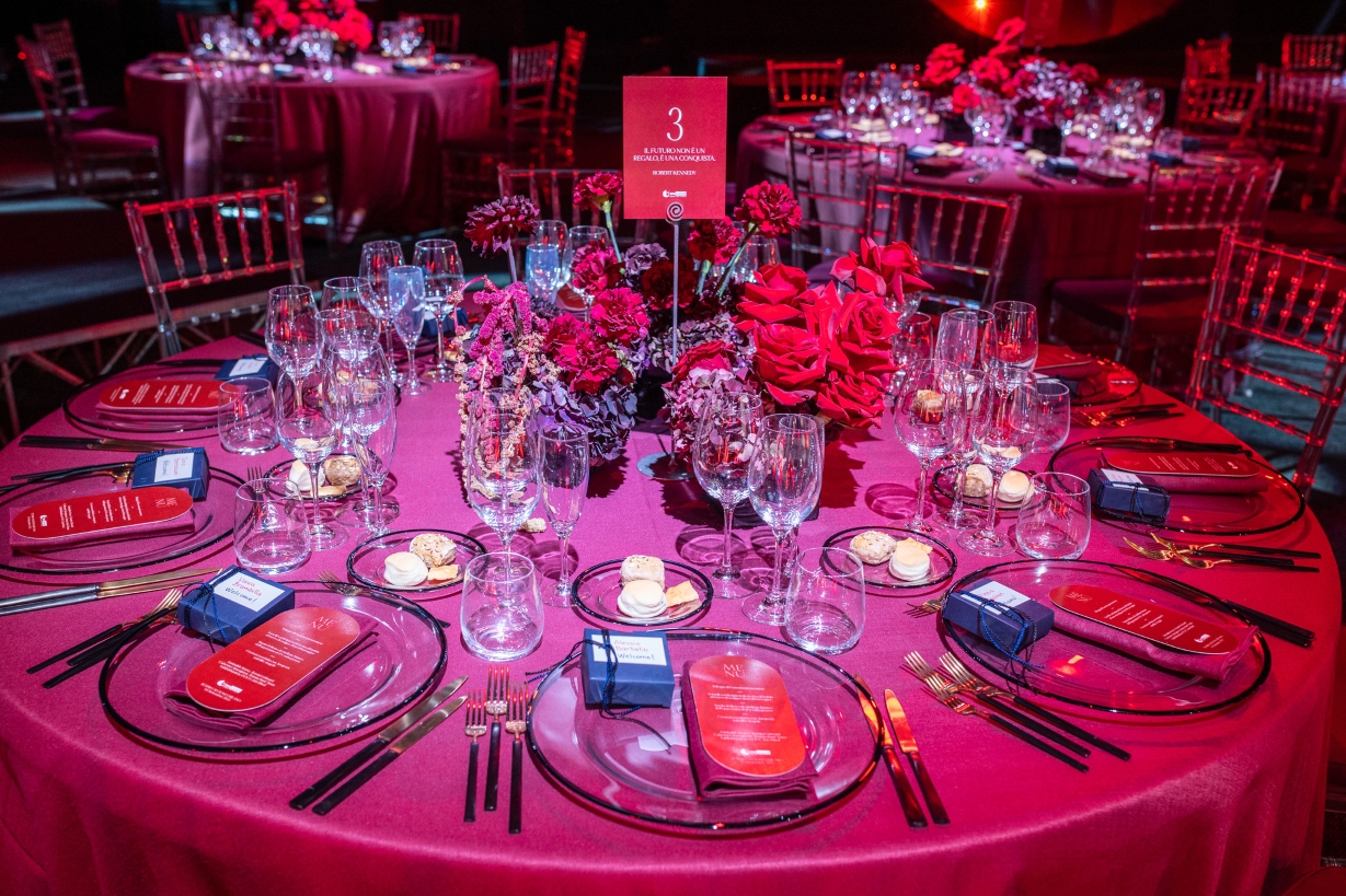Round table elegantly set with red tablecloth, candles, glasses and central red flowers - ACCAELLE Events | Organizzazione eventi e Wedding planner