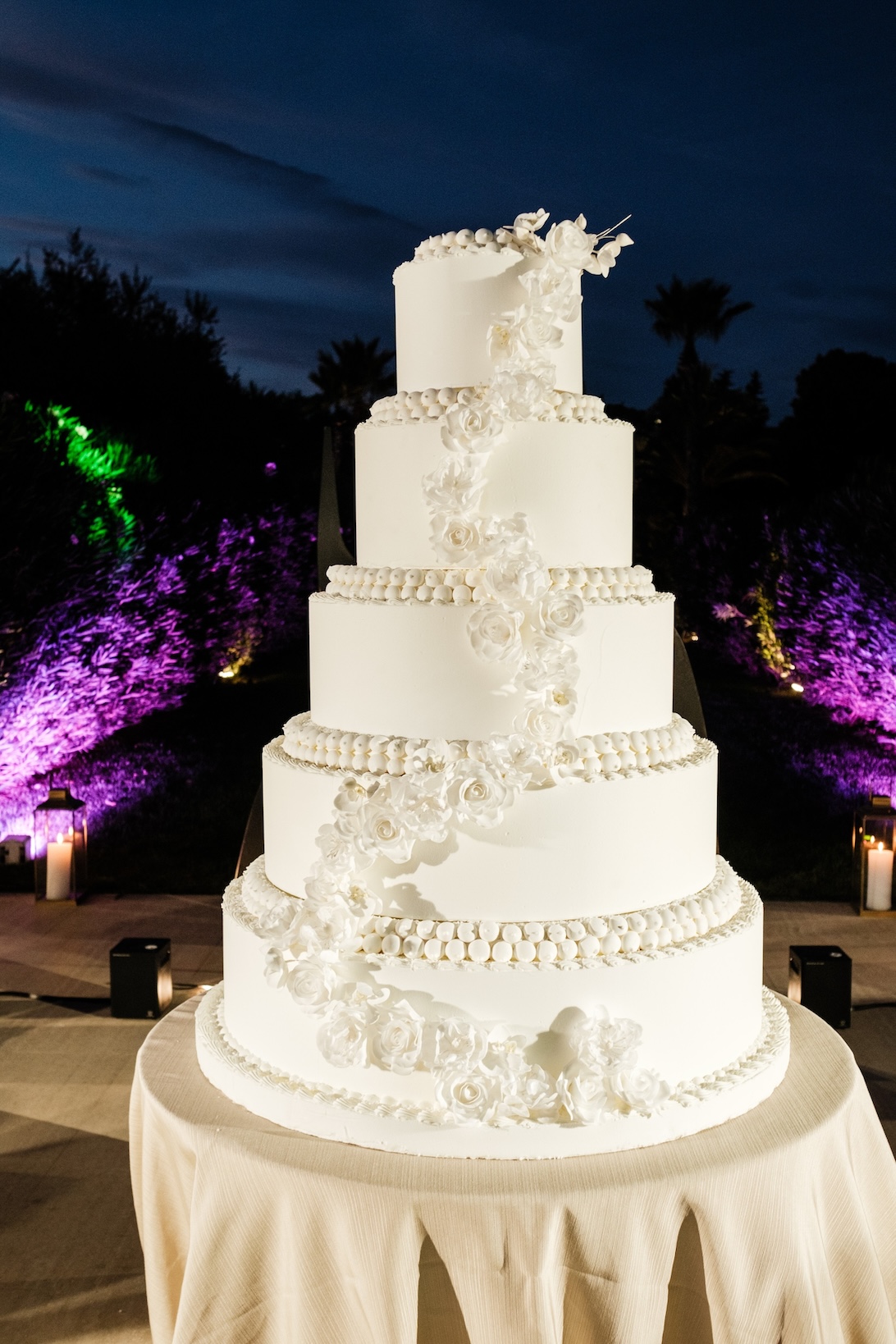 A 5-tier wedding cake decorated with white spheres and white roses against a meadow backdrop in the evening. - ACCAELLE Events | Organizzazione eventi e Wedding planner
