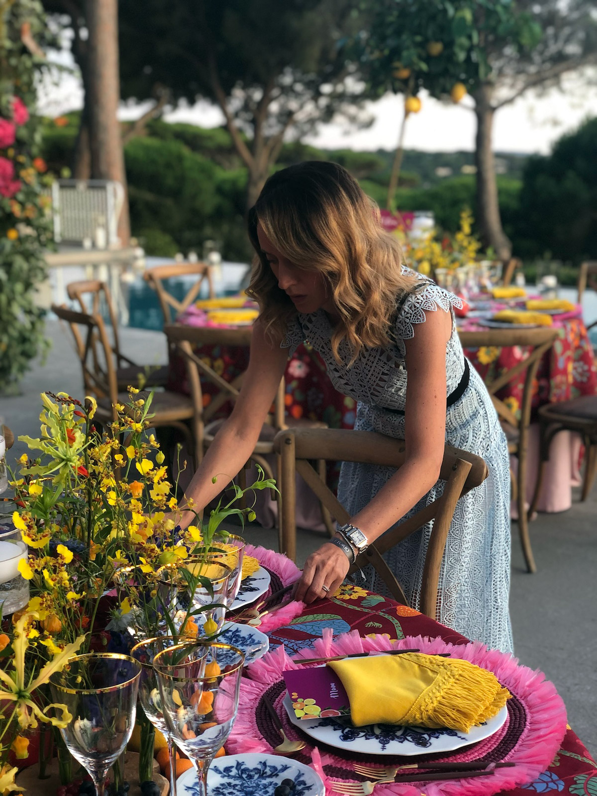 A woman finishing the details of the dishes on a decorated table in a garden. - ACCAELLE Events | Organizzazione eventi e Wedding planner