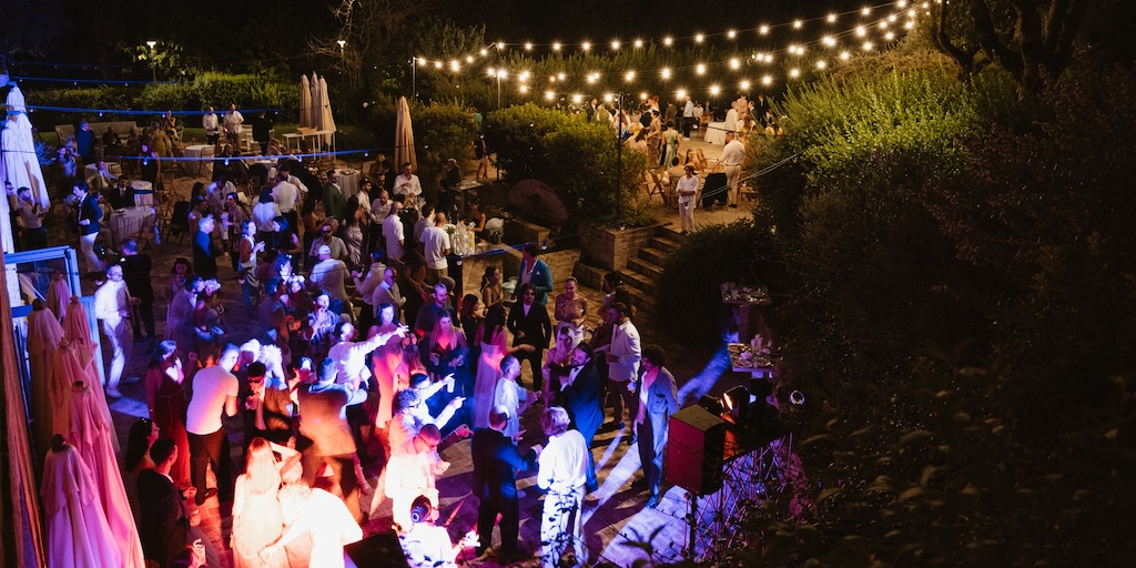 An overhead shot of guests dancing in an area lit by blue and pink lights. - ACCAELLE Events | Organizzazione eventi e Wedding planner