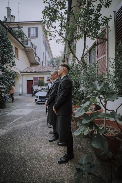 Men in elegant black suits posing in the courtyard with a Bentley Continental GT in the background - ACCAELLE Events | Organizzazione eventi e Wedding planner