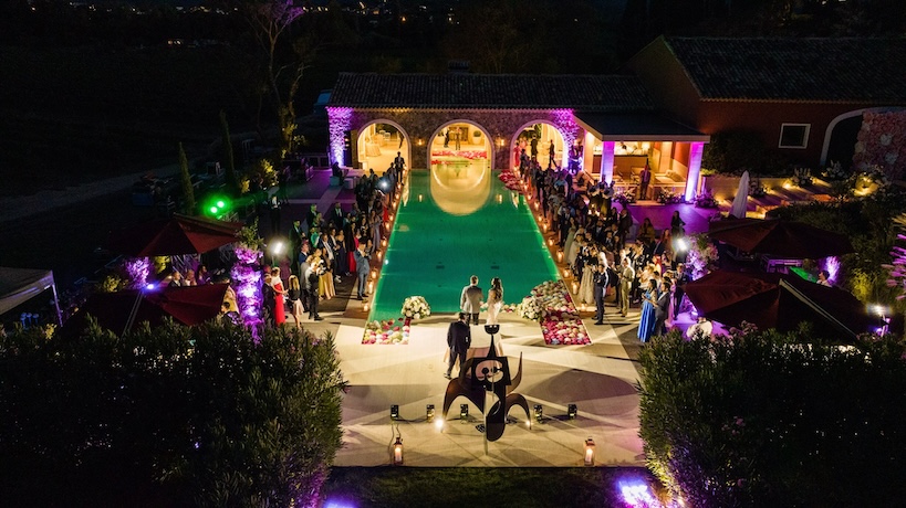 View from above of the structure with swimming pool and purple lights, with guests and the newlyweds in the evening - ACCAELLE Events | Organizzazione eventi e Wedding planner
