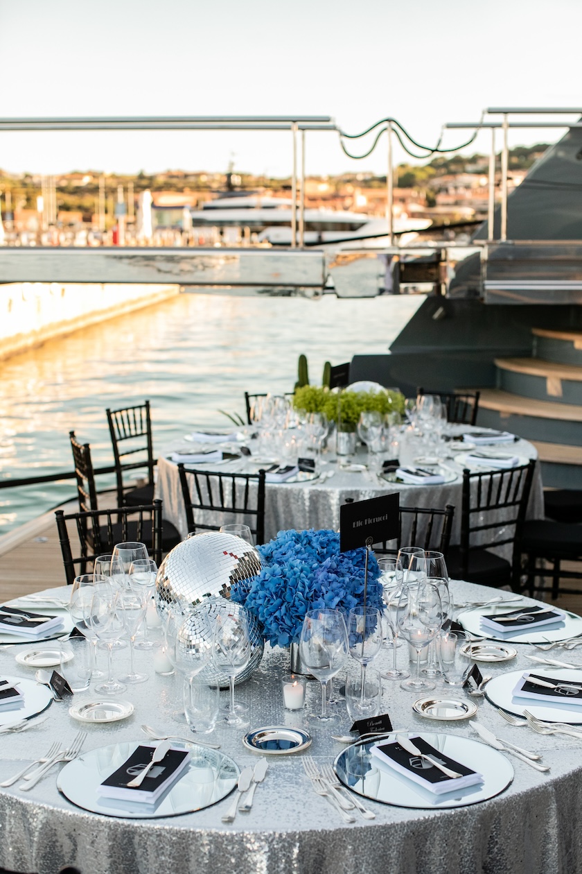 View of a round table on the outer deck of the ship with the sea and coast in the background. - ACCAELLE Events | Organizzazione eventi e Wedding planner