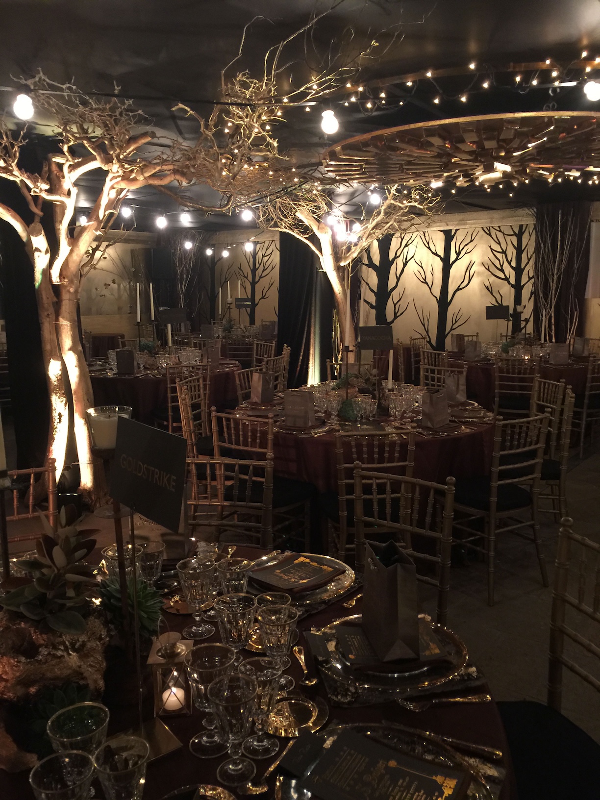 Allestimento scenografico per cena di Bvlgari, caratterizzato da alberi decorativi, luci soffuse e tavoli rotondi - ACCAELLE Events | Organizzazione eventi e Wedding planner
