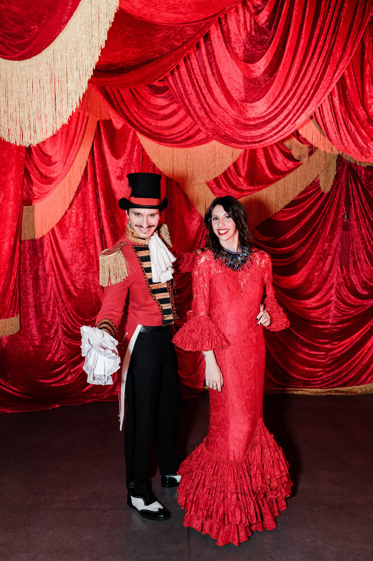 Artisti vesti con abiti circensi che posano abbracciati sotto dei tendaggi rossi e oro - ACCAELLE Events | Organizzazione eventi e Wedding planner