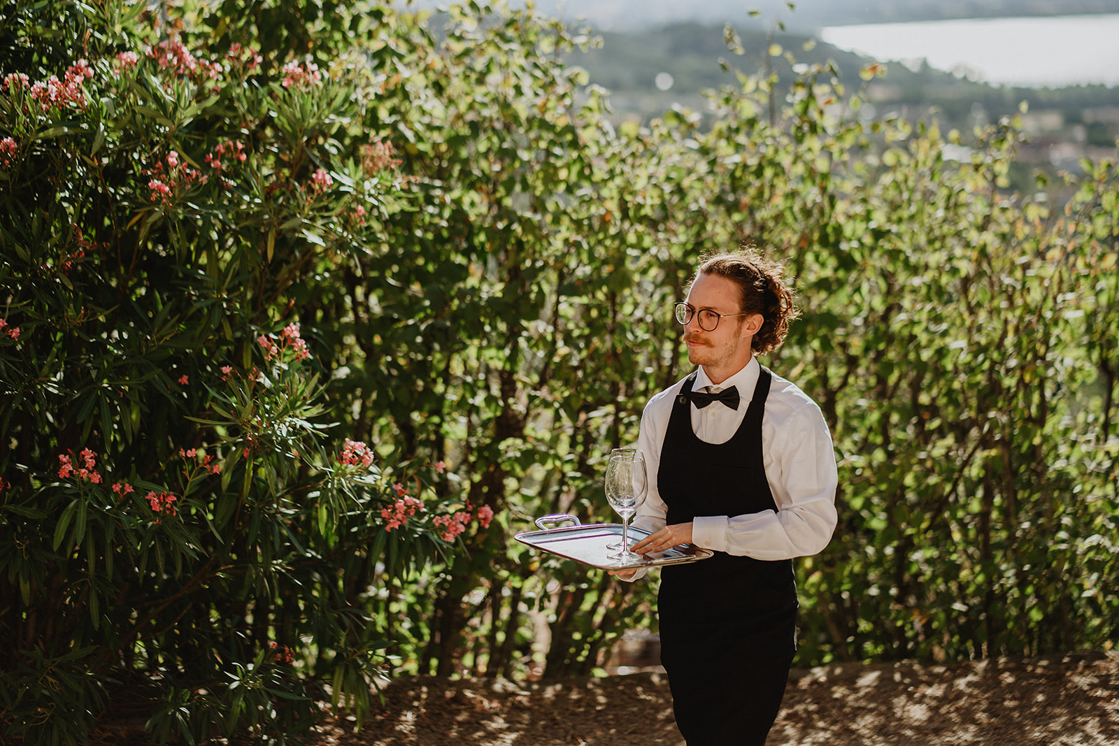Cameriere in divisa formale ed elegante cammina tra il verde portando un vassoio d'argento. - ACCAELLE Events | Organizzazione eventi e Wedding planner