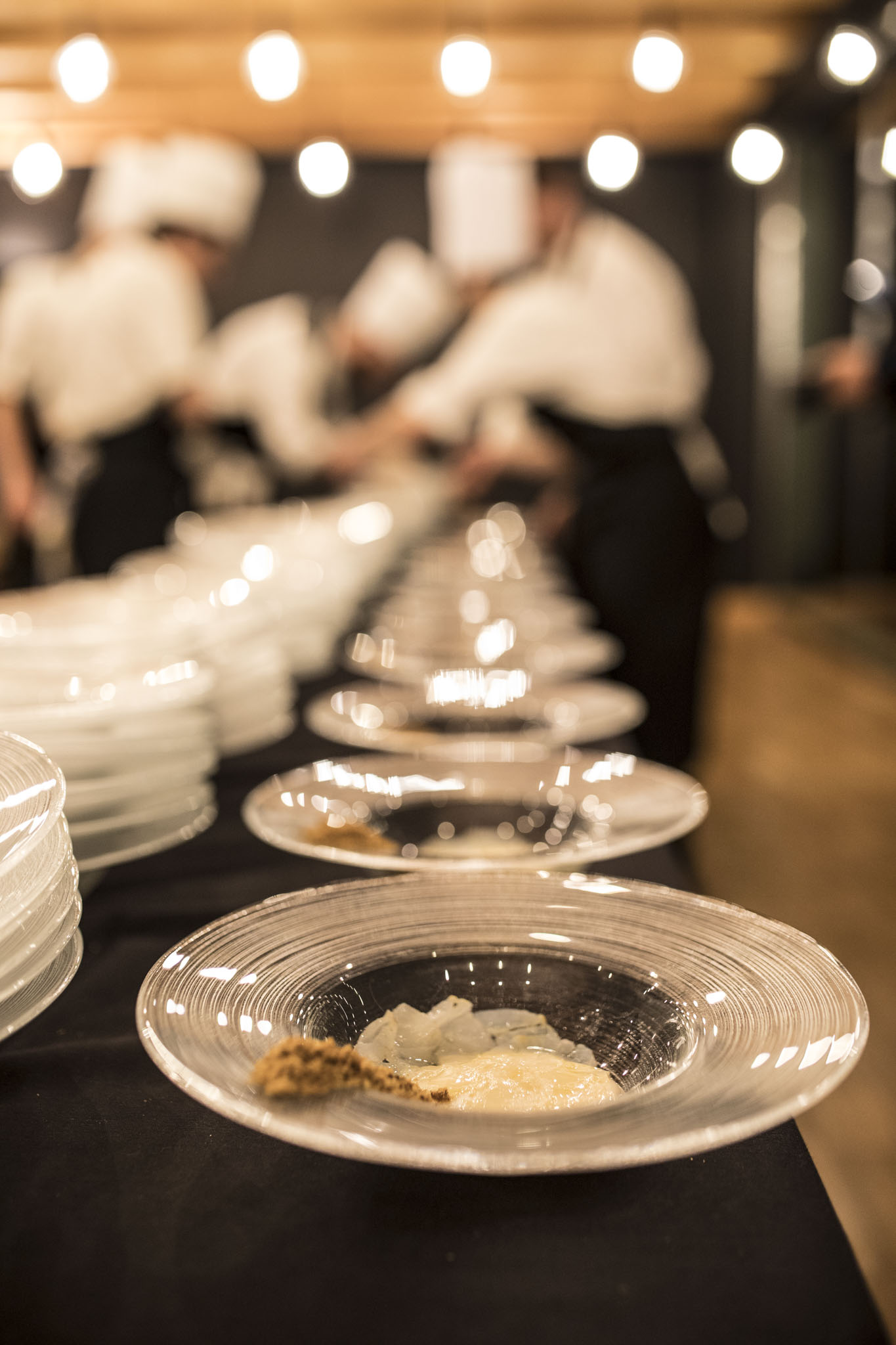 Chef in cucina che impiattano con precisione una fila di piatti eleganti per un evento. - ACCAELLE Events | Organizzazione eventi e Wedding planner