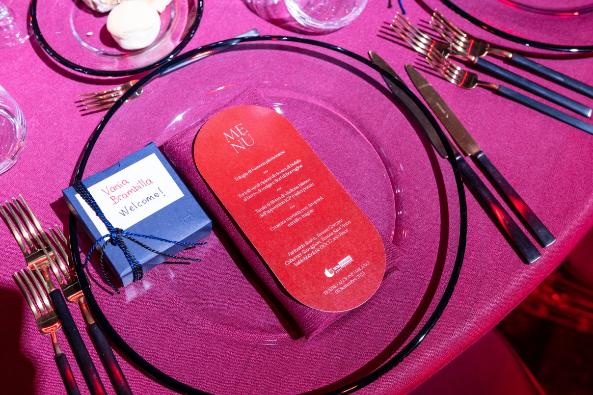 Dettaglio della mise en place con piatto trasparente, menu rosso e un piccolo regalo blu. - ACCAELLE Events | Organizzazione eventi e Wedding planner