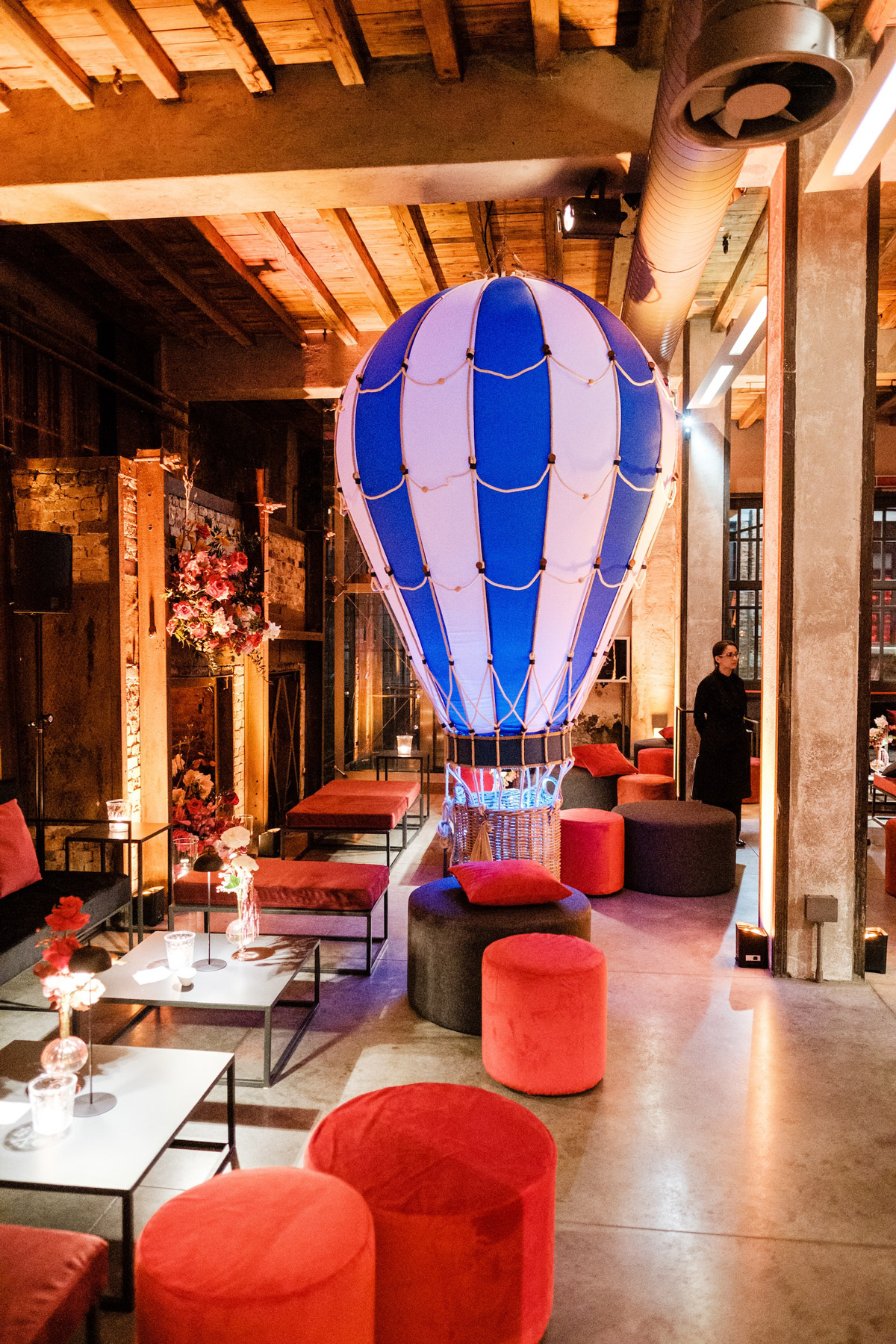 Dettaglio di una sala cin tavoli bassi, pouf rossi cilindrici e mongolfiera bianco blu sullo sfondo - ACCAELLE Events | Organizzazione eventi e Wedding planner