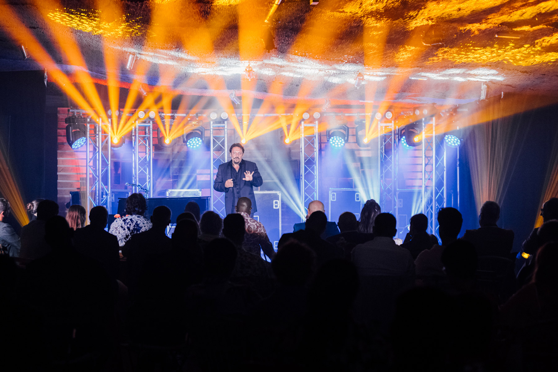 Enrico Brignano che parla al pubblico su palco illuminato - ACCAELLE Events | Organizzazione eventi e Wedding planner