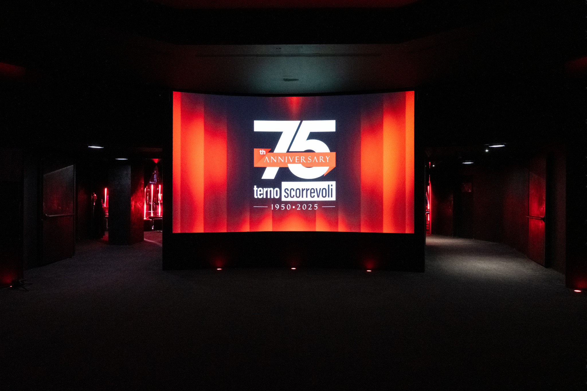 Grande schermo per eventi incorniciato da tende rosse in una sala buia per 75° anniversario - ACCAELLE Events | Organizzazione eventi e Wedding planner