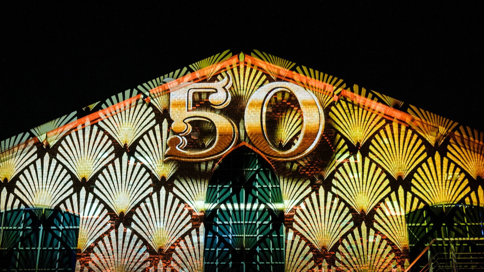 Numero 50 dorato tridimensionale su una parete con pattern geometrico illuminato. - ACCAELLE Events | Organizzazione eventi e Wedding planner