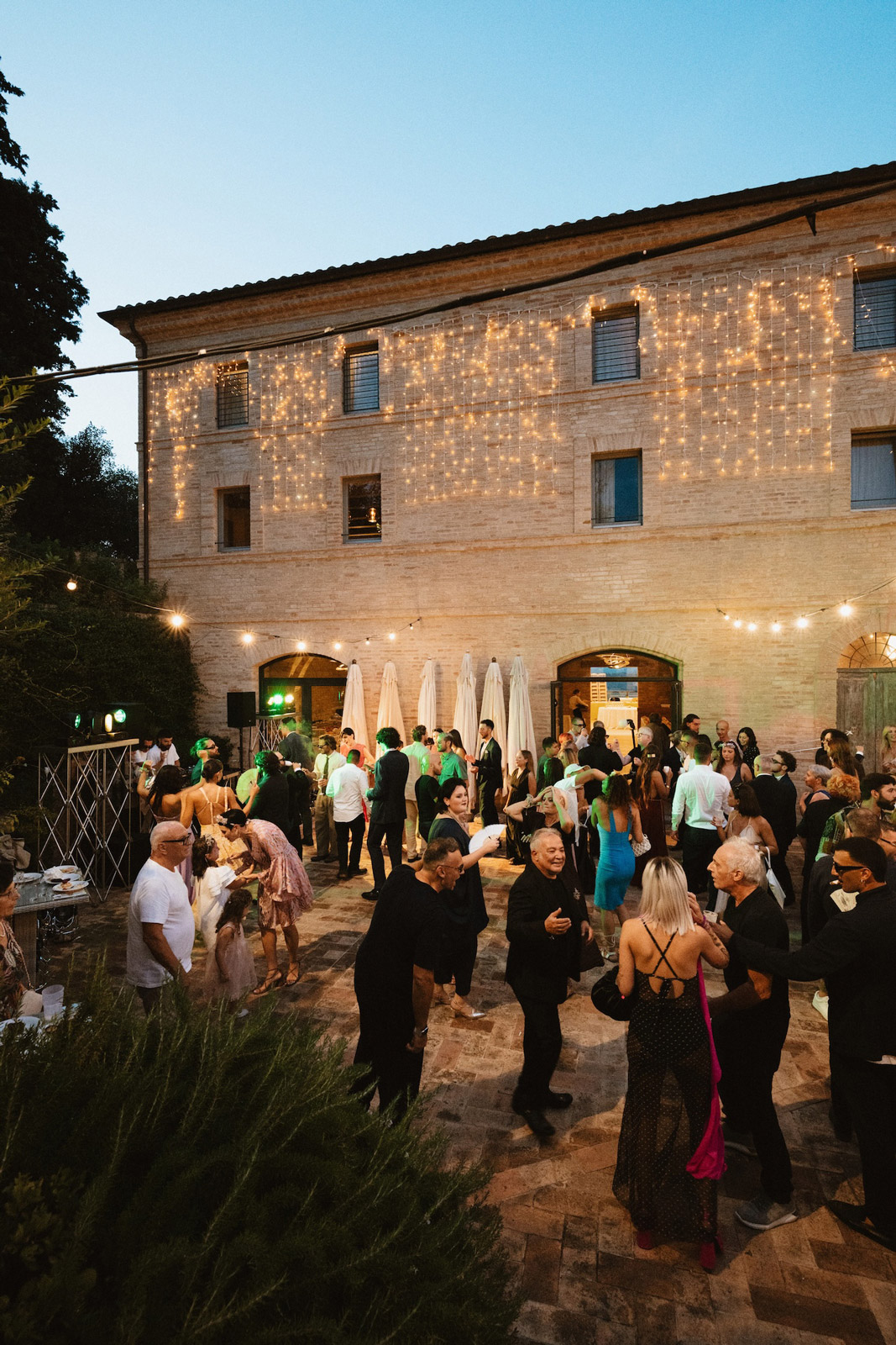 Ospiti matrimonio in momento serale, edificio addobbato con luci calde sullo sfondo - ACCAELLE Events | Organizzazione eventi e Wedding planner