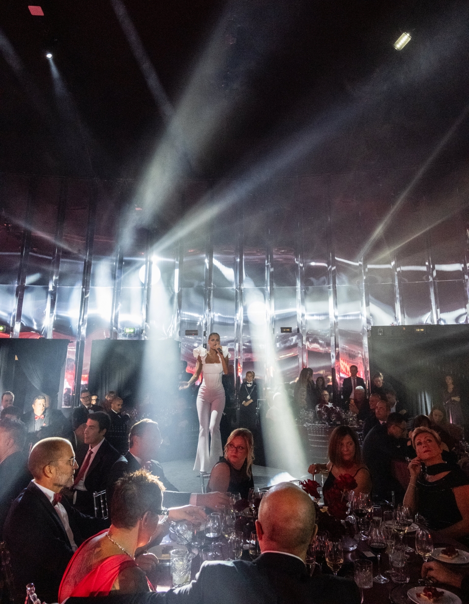 Ospiti seduti ai tavoli di un gala sotto intensi fasci di luce bianca scenografica - ACCAELLE Events | Organizzazione eventi e Wedding planner
