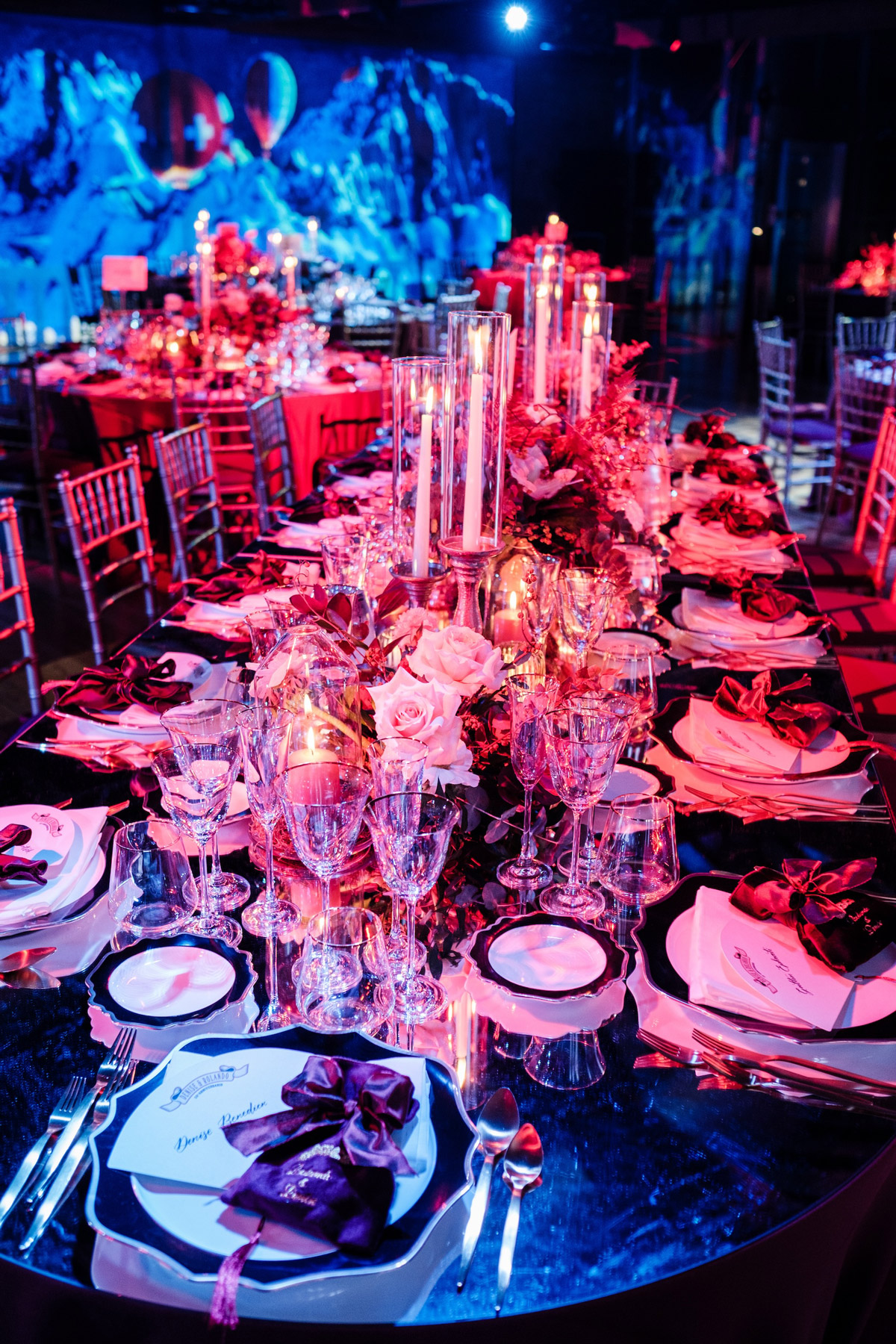 Primo piano di un lungo tavolo elegantemente con dettagli floreali e candela al centro illuminato da una luce rossa - ACCAELLE Events | Organizzazione eventi e Wedding planner