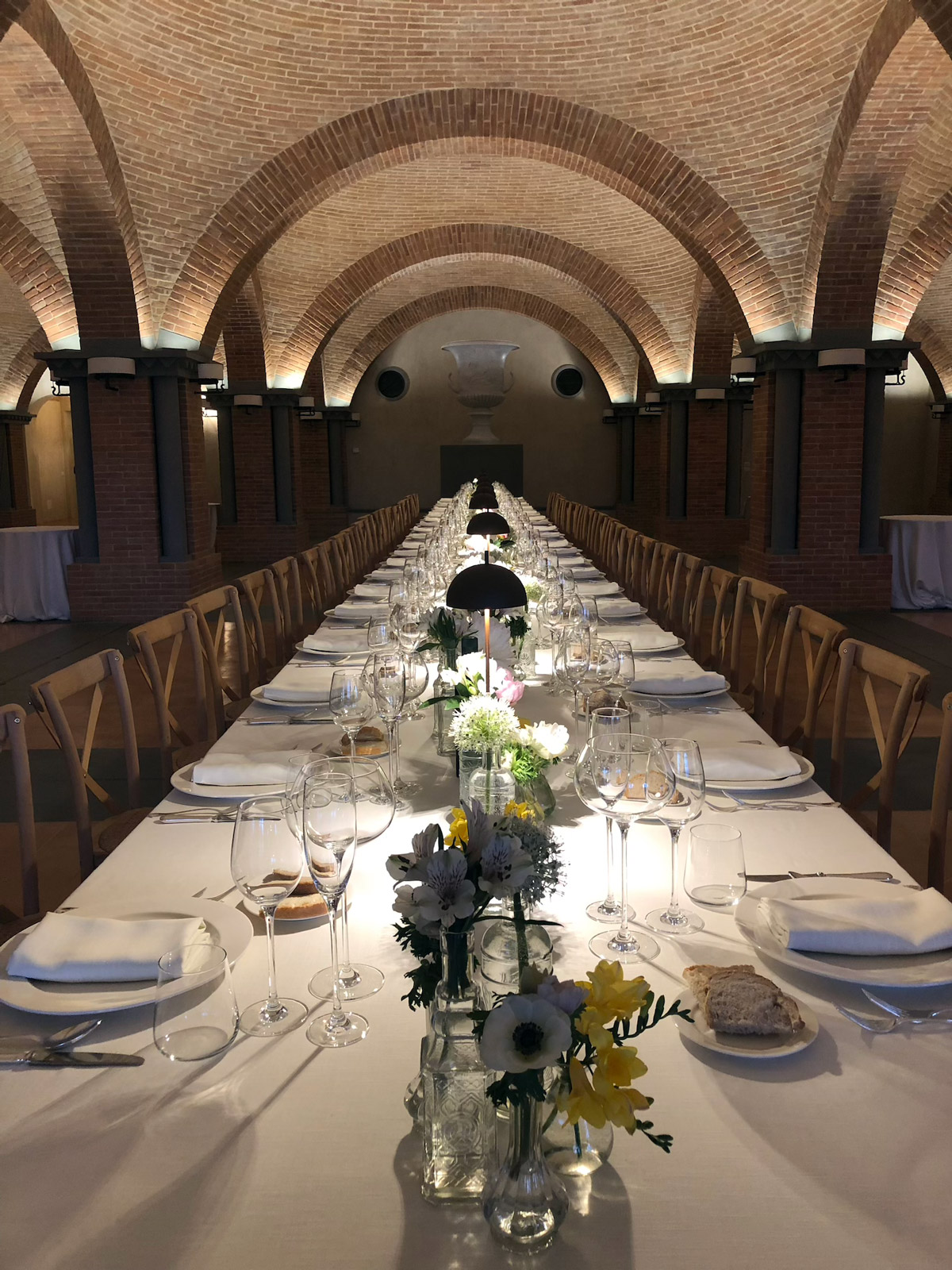 Prospettiva centrale di una lunga tavola apparecchiata in una galleria d'epoca con archi. - ACCAELLE Events | Organizzazione eventi e Wedding planner